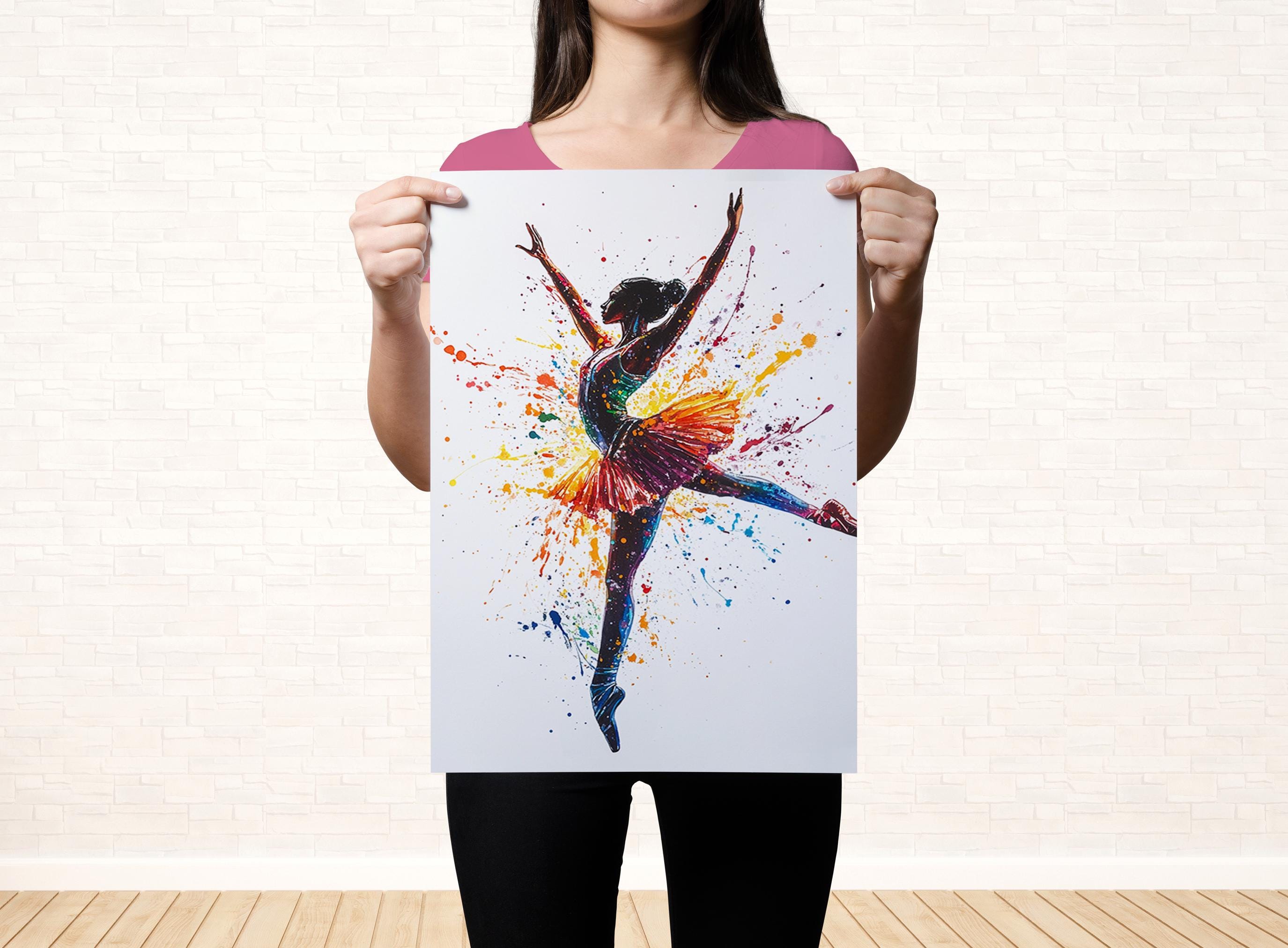 A woman is holding up a colorful painting of a ballerina with her arms raised, against a white brick wall background.