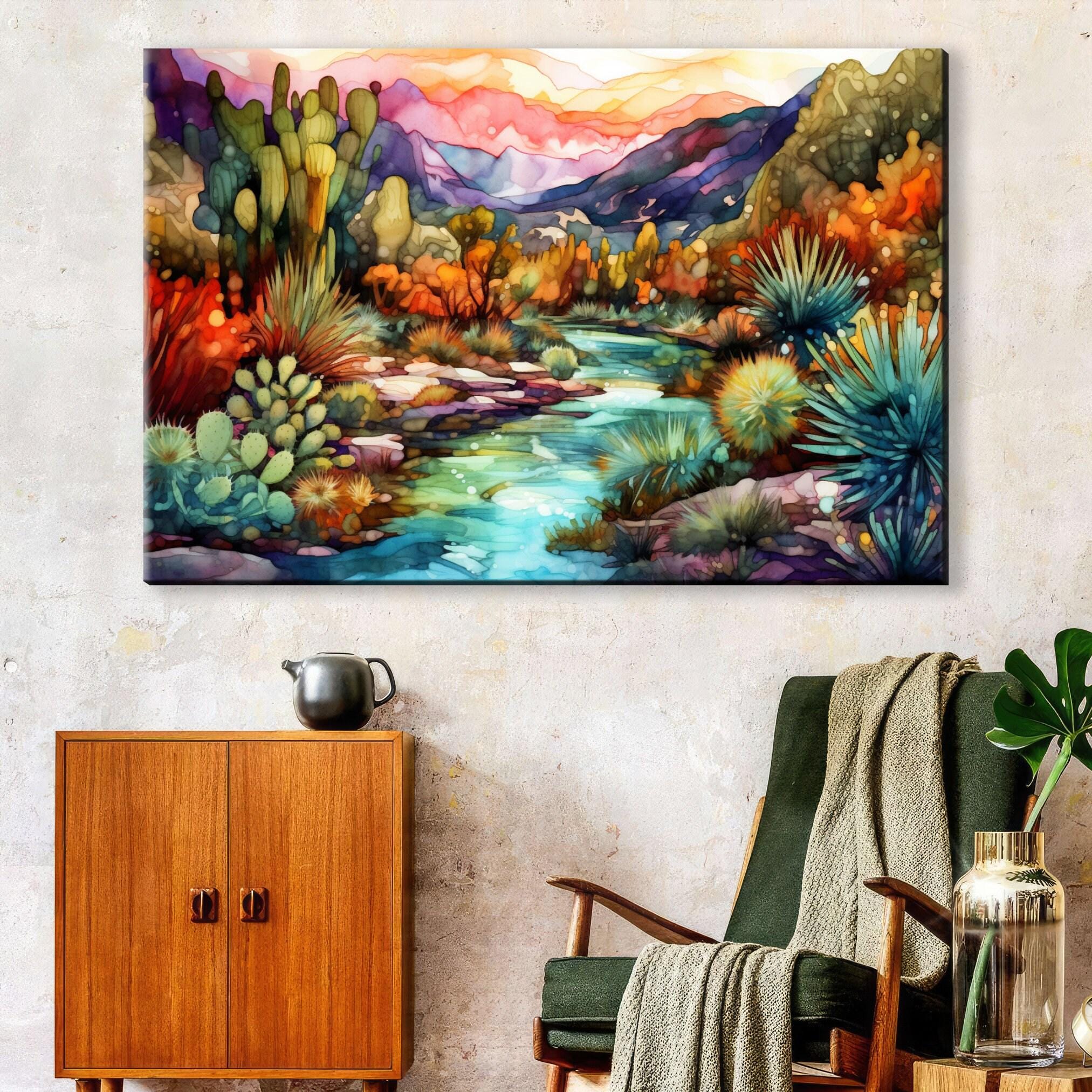 a vibrant, colorful painting of a desert landscape with mountains, cacti, and a winding river. The painting is hung on a wall above a wooden cabinet and a green armchair, creating a cozy and artistic atmosphere in the room.