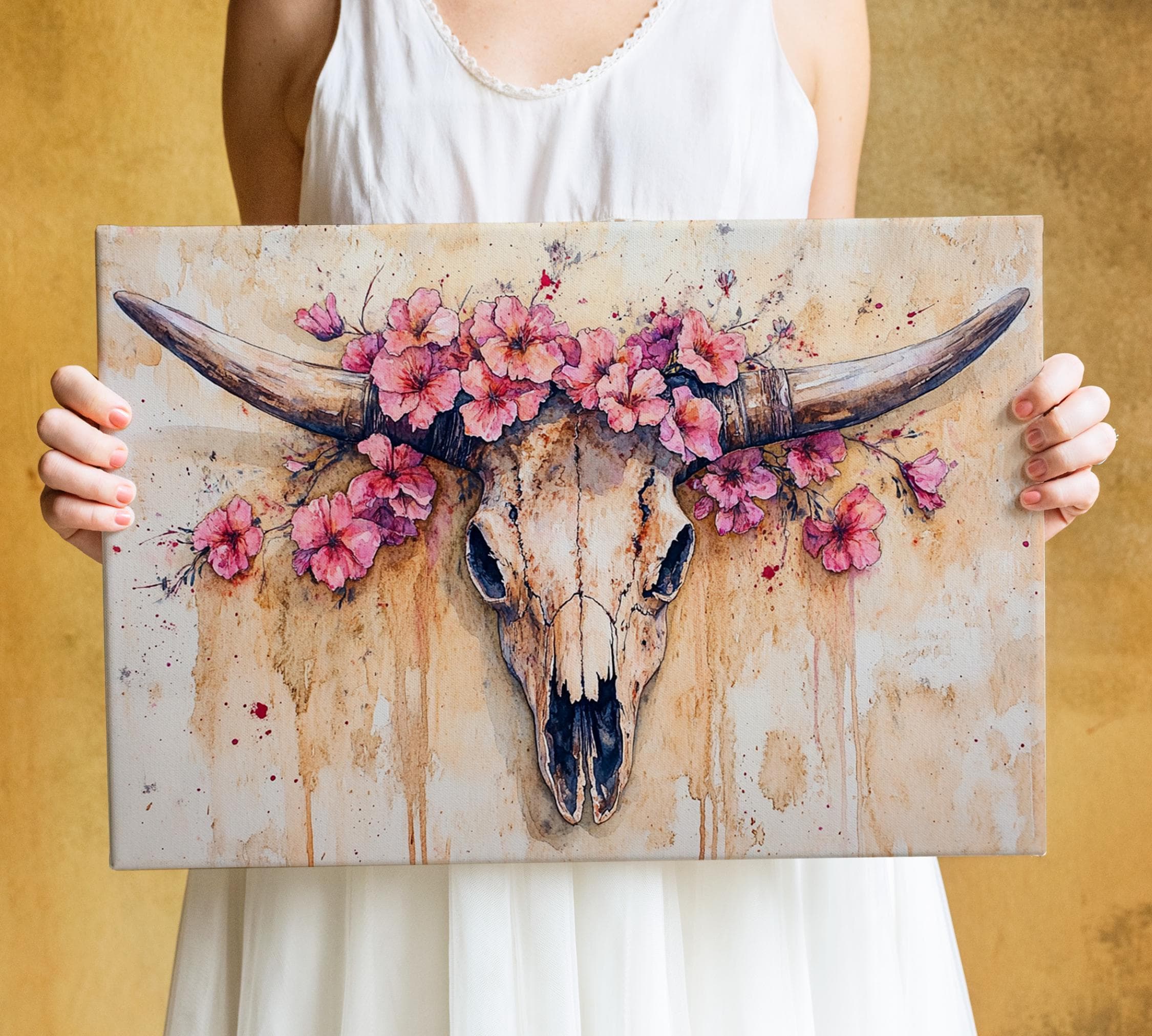 A woman holds a framed artwork featuring a painted skull with horns and pink flowers.