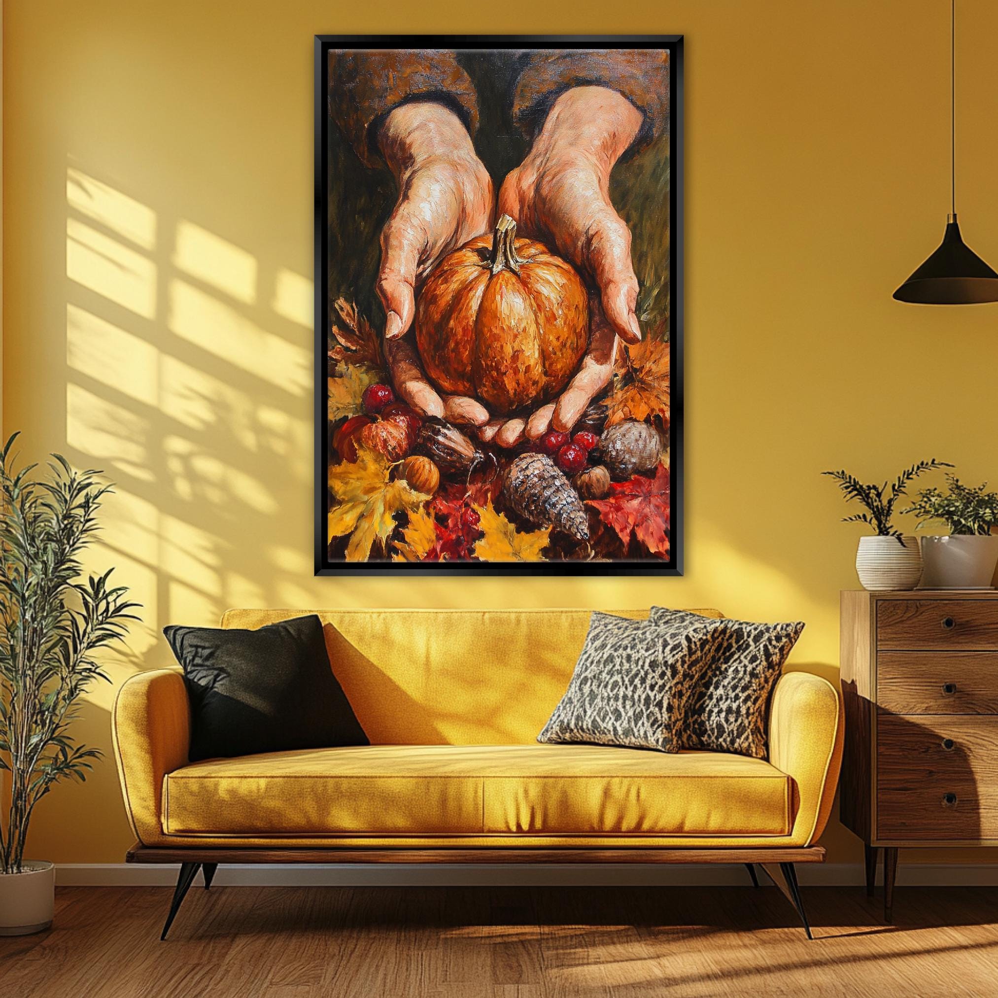 A large painting of a pair of hands holding a pumpkin is displayed on the wall above a yellow couch with decorative pillows.