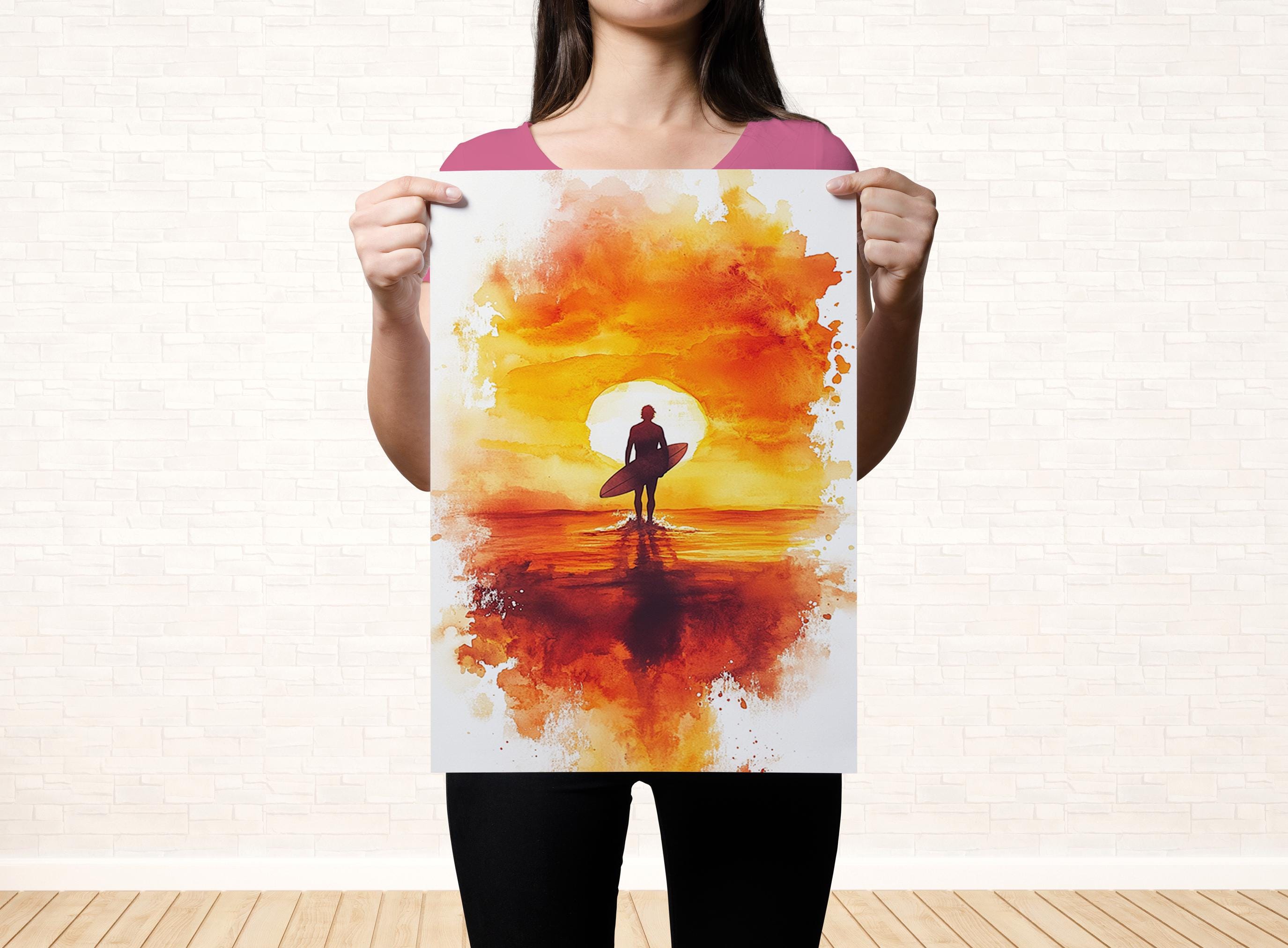 A woman holds up a watercolor painting depicting a surfer on a beach at sunset.
