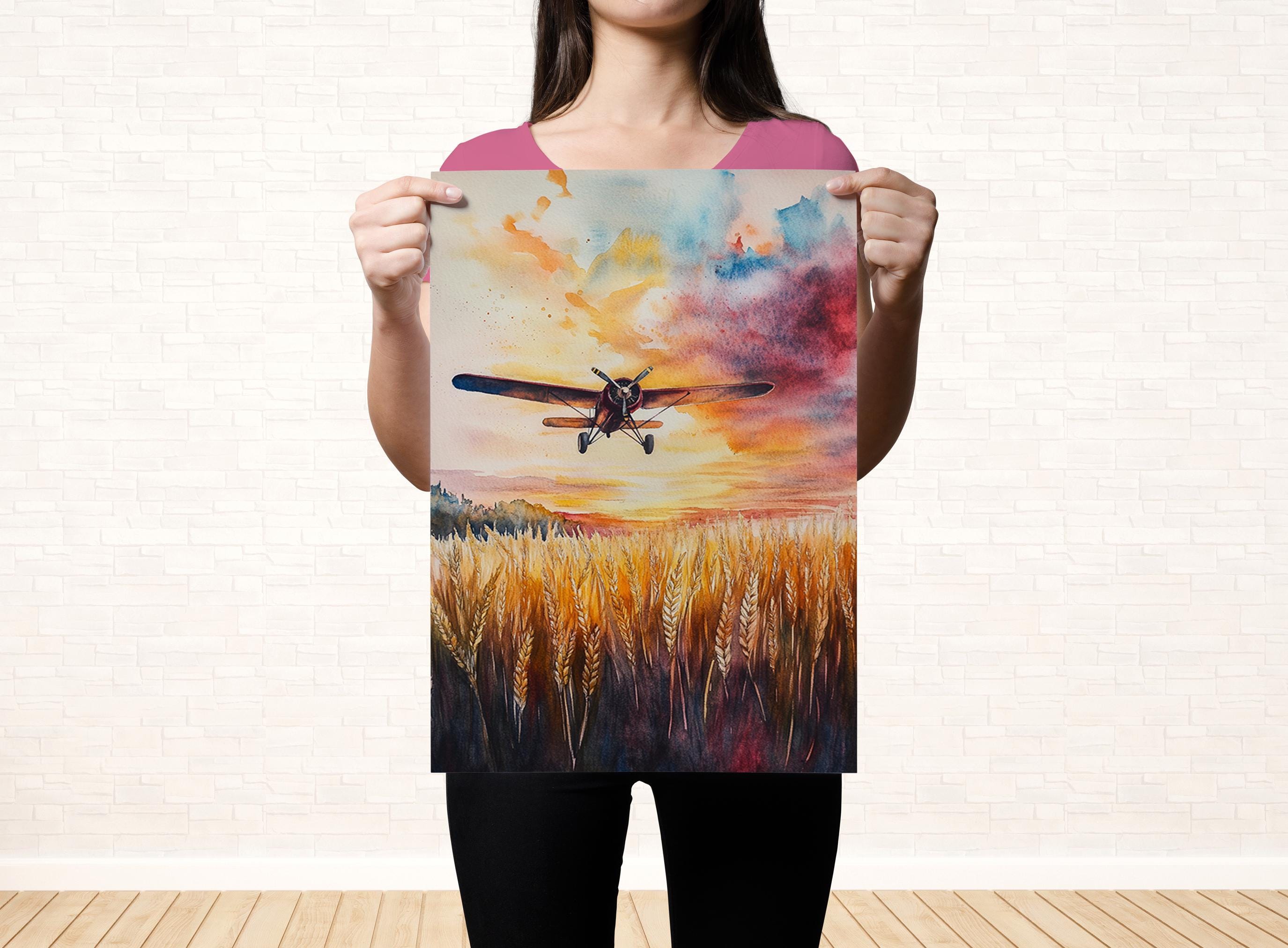 A woman holds up a framed painting depicting a colorful sunset over a field of tall grass.