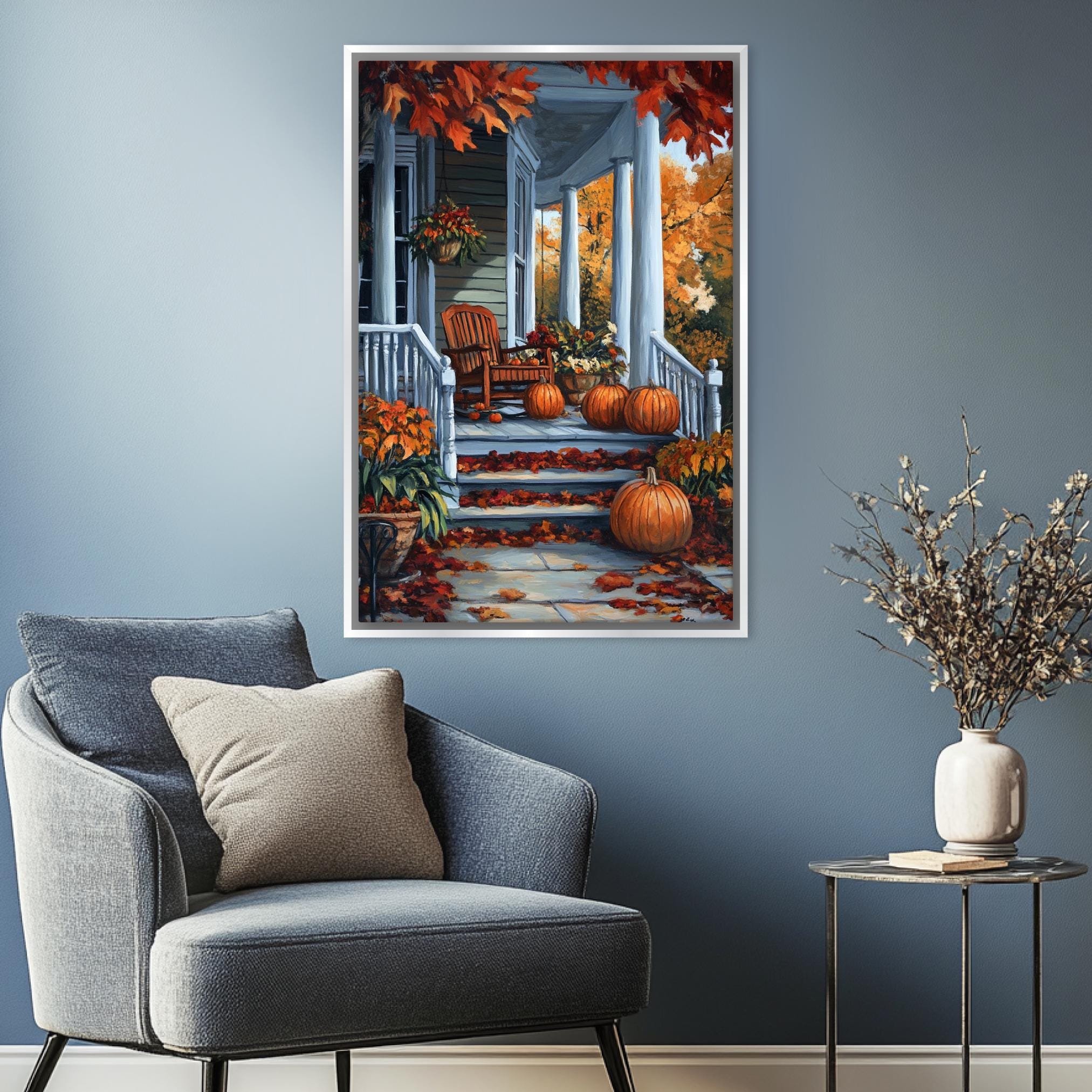 a cozy living room with a gray armchair, a small side table, and a framed painting of a porch with autumn decorations hanging on the wall.