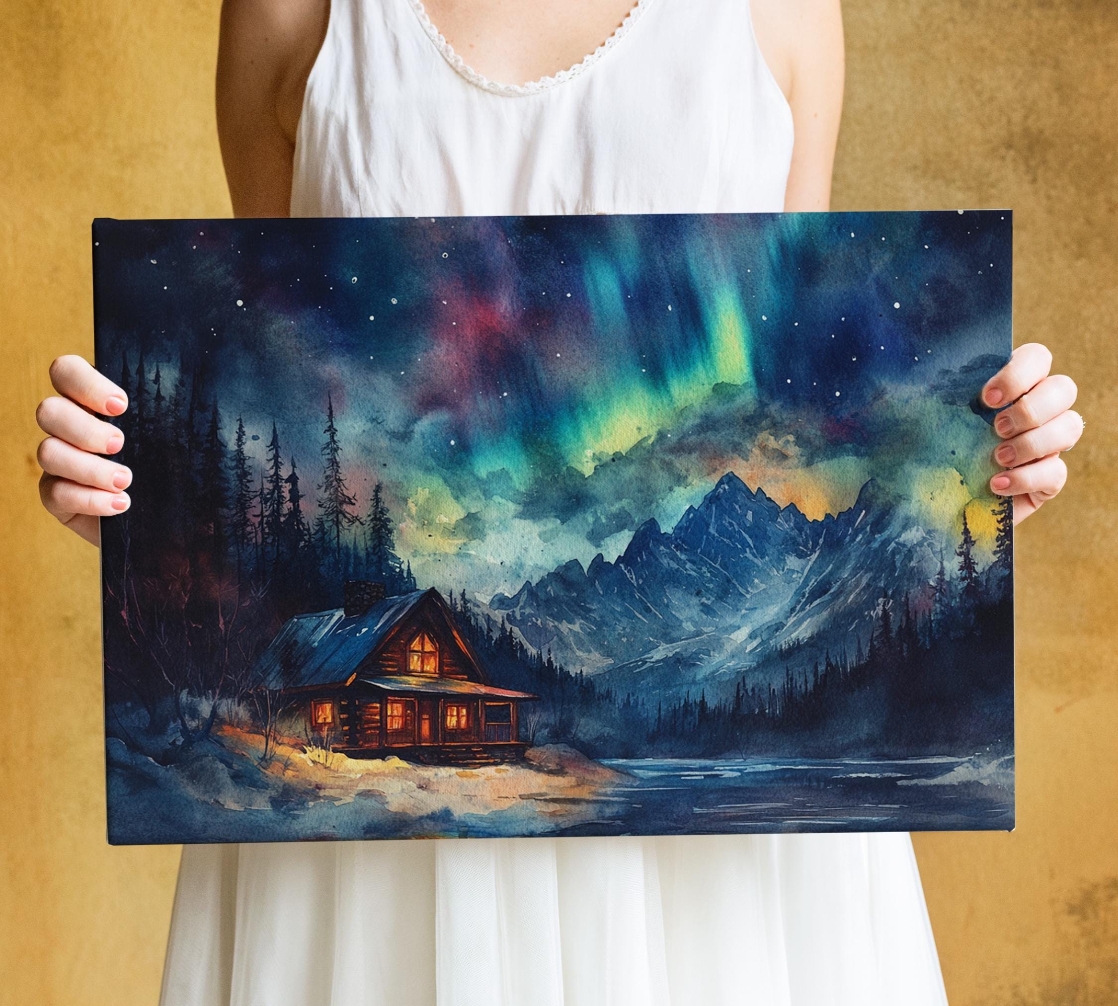 A woman holds a painting of a cabin in a snowy mountain landscape, with a night sky filled with stars and the northern lights above.