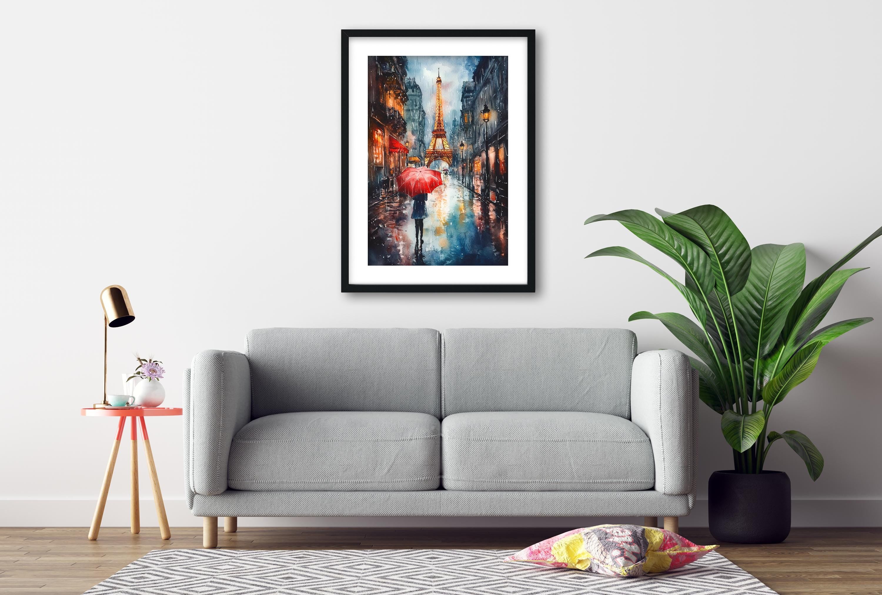 a gray sofa, a framed painting of a rainy city street with a red umbrella, a small table with a lamp, and a potted plant.