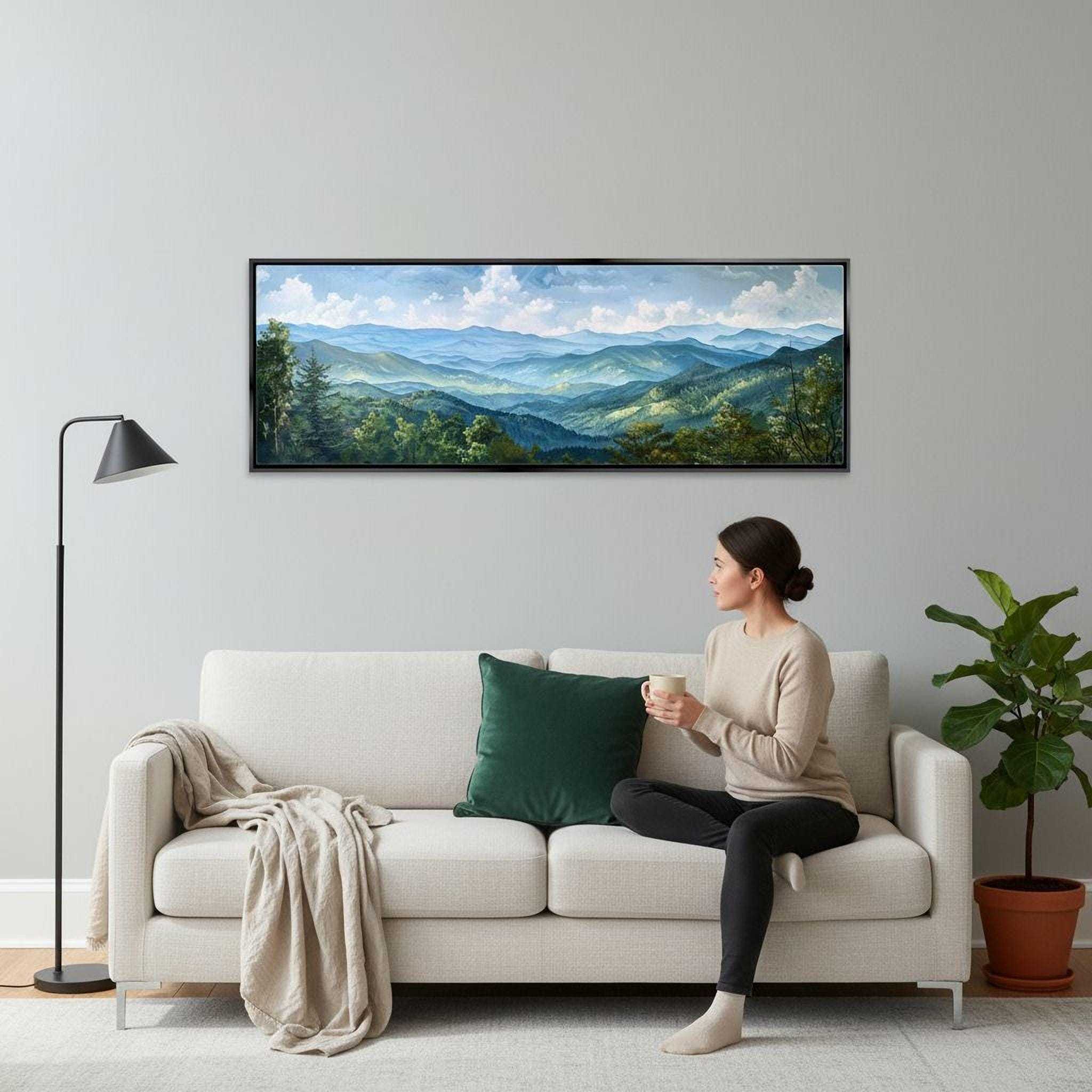 A woman sits on a white couch, holding a coffee mug and looking out a window at a mountainous landscape.