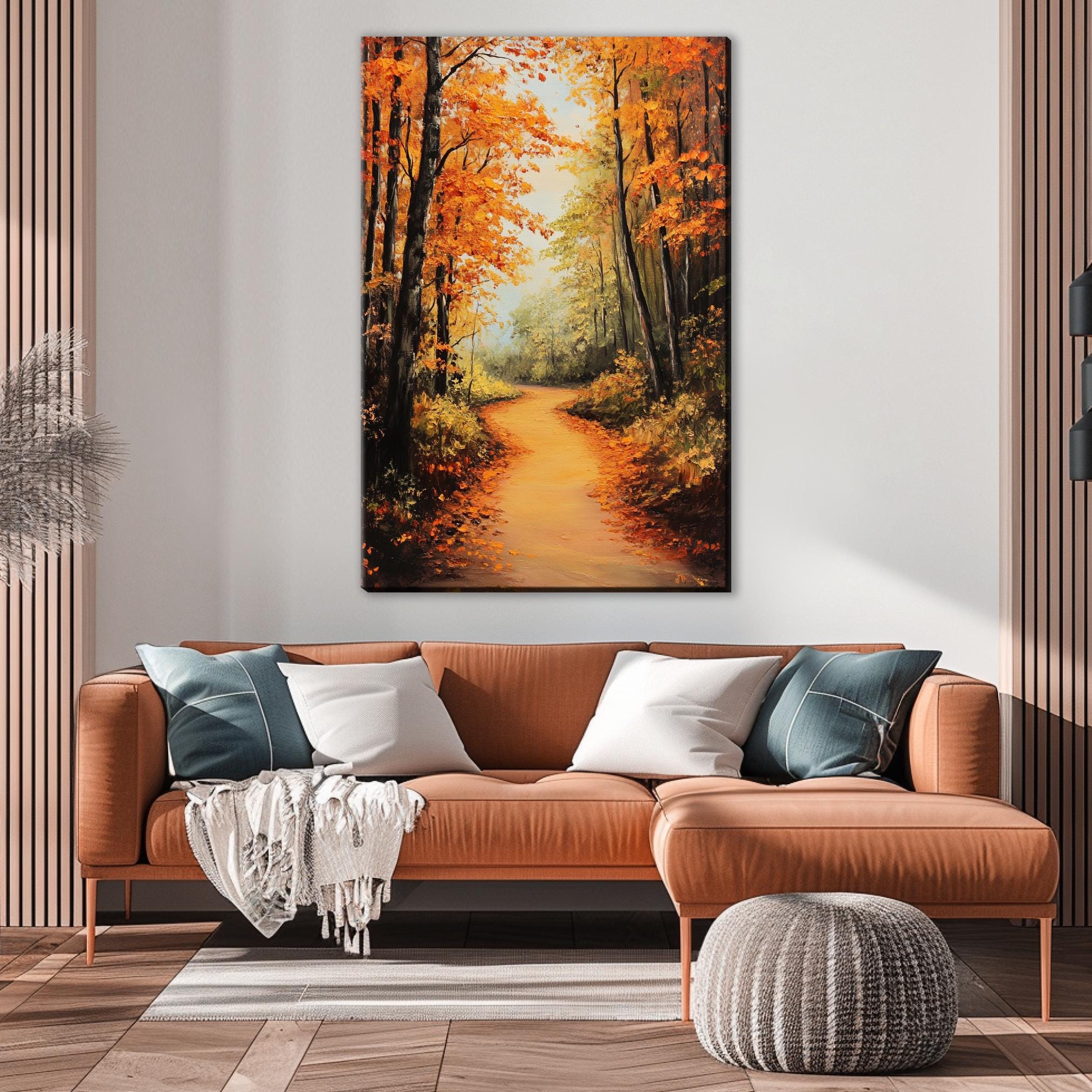 a cozy living room with a large painting of a forest path on the wall above a brown leather sofa. The painting depicts a winding path surrounded by trees with orange leaves, creating a warm and inviting atmosphere.