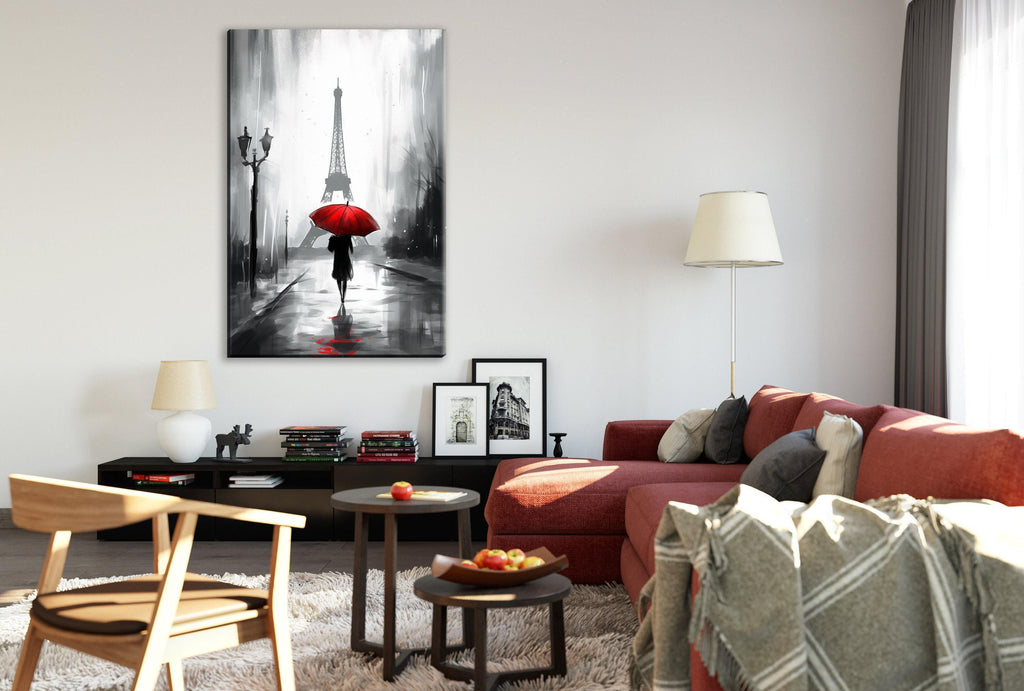 a cozy living room with a large painting of a person walking with an umbrella in the rain hanging on the wall. The room is furnished with a red couch, a wooden chair, and a coffee table with a bowl of fruit. The overall color scheme of the room is predominantly red and white, with accents of gray and black.
