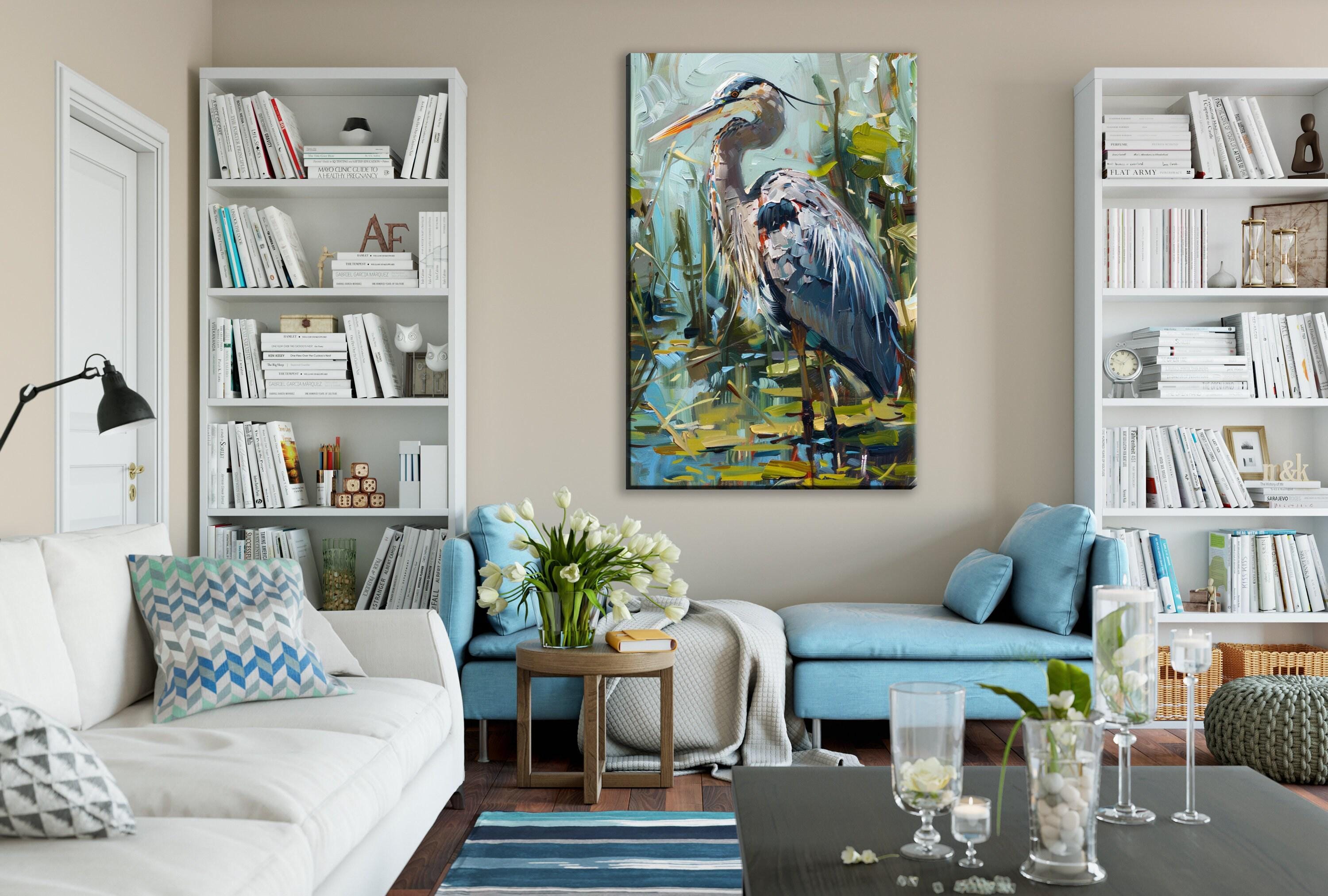 a cozy living room with a large painting of a blue heron on the wall. The room is furnished with a white sofa, a blue armchair, and a wooden coffee table. The walls are decorated with white bookshelves, and the room is illuminated by a lamp. The overall atmosphere of the room is calm and inviting, with a touch of nature represented by the painting of the heron.