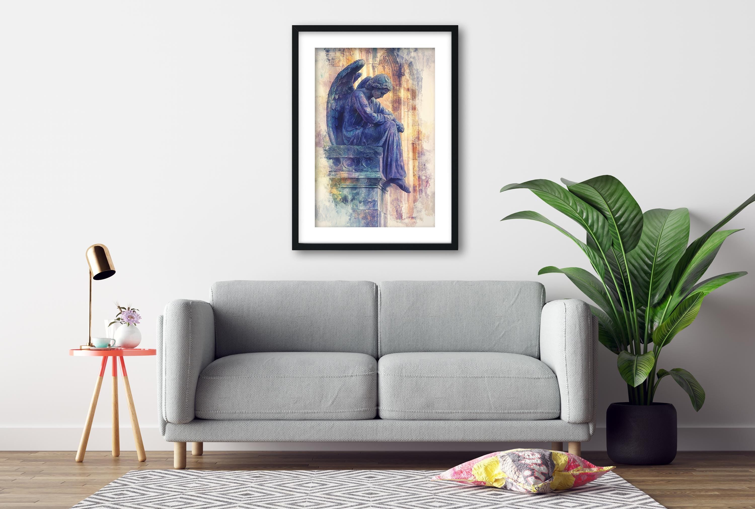 a gray sofa, a framed painting of an angel, a small table with a lamp, and a potted plant, all arranged in a living room setting.