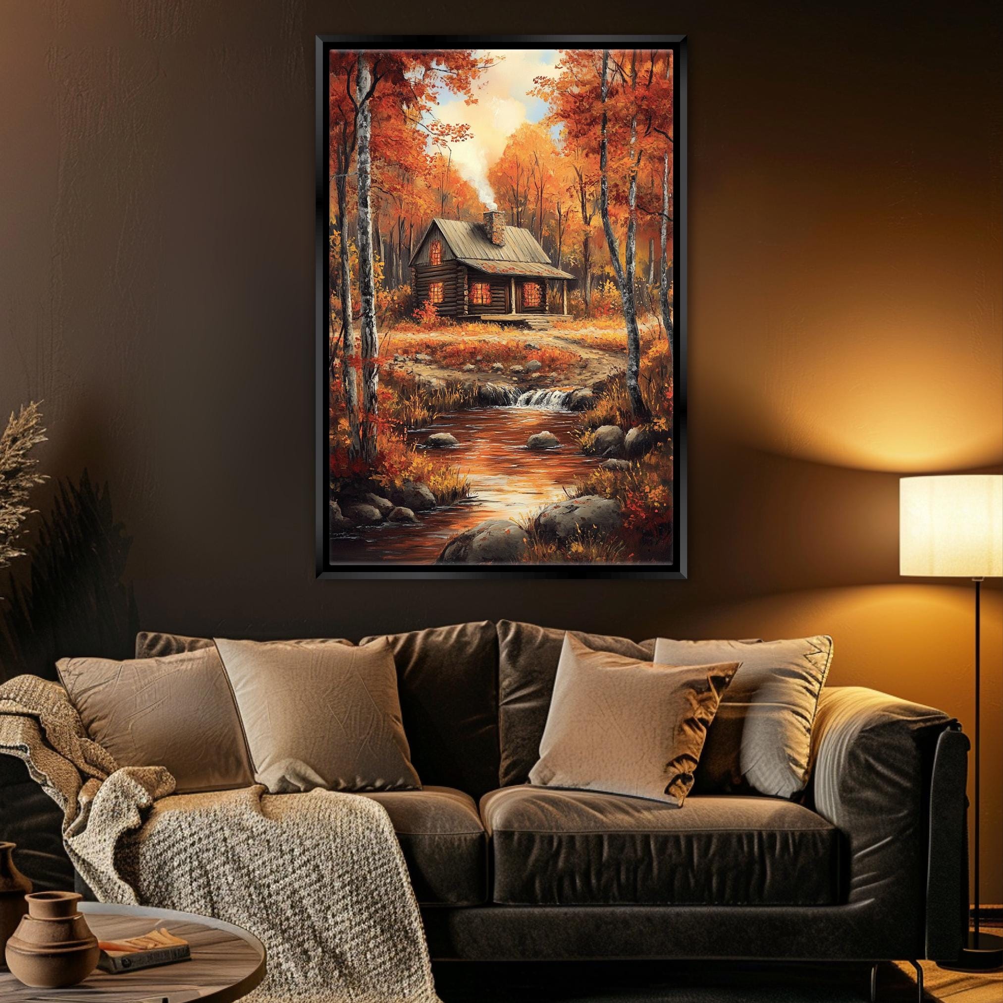 a cozy living room with a large framed painting of a cabin nestled in a forest, surrounded by autumn foliage. The painting is hung on the wall above a comfortable couch with plush pillows and a warm throw blanket. The room is dimly lit, creating a warm and inviting atmosphere.