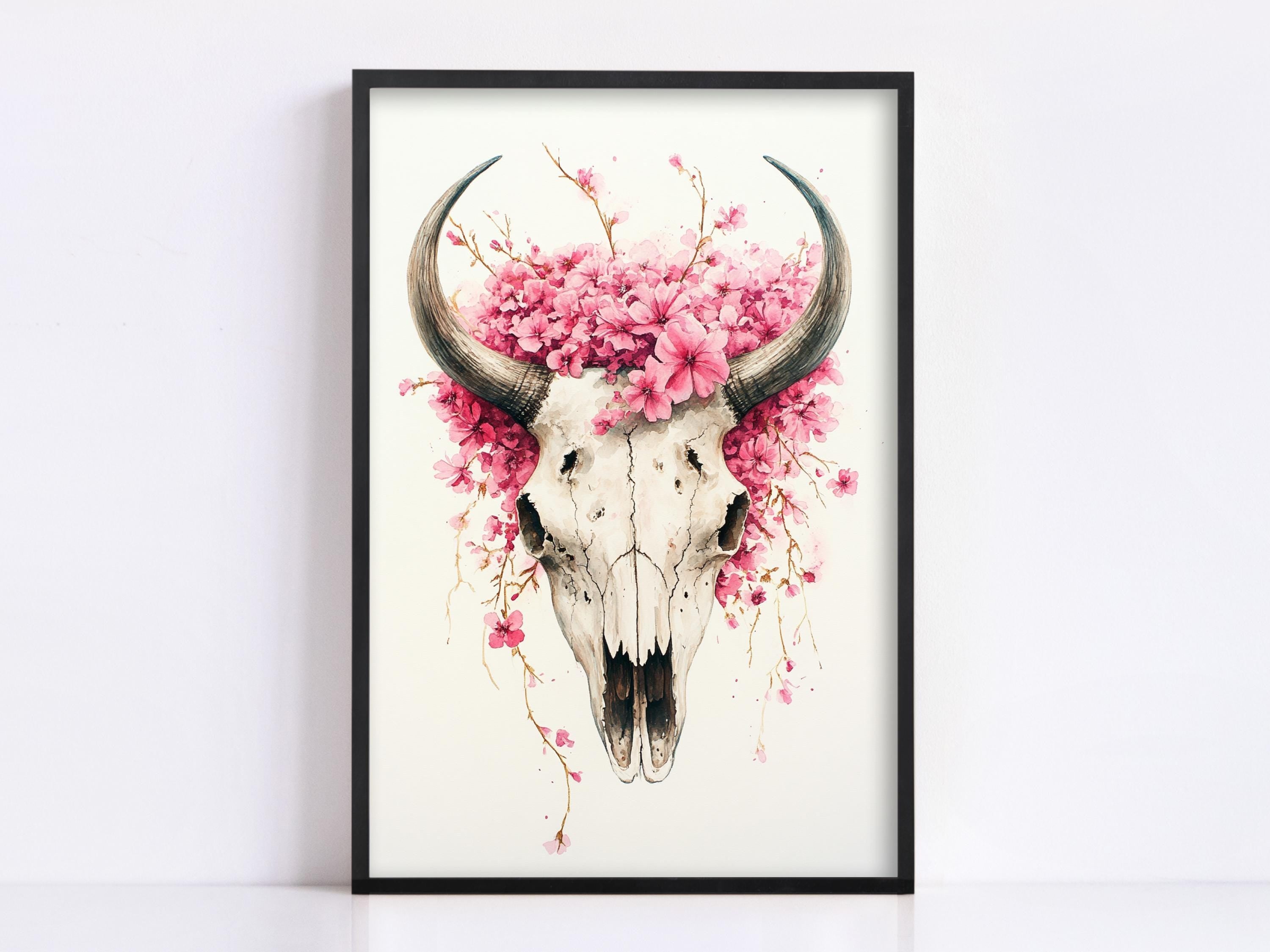 A framed artwork depicting a skull with large horns, surrounded by pink flowers.