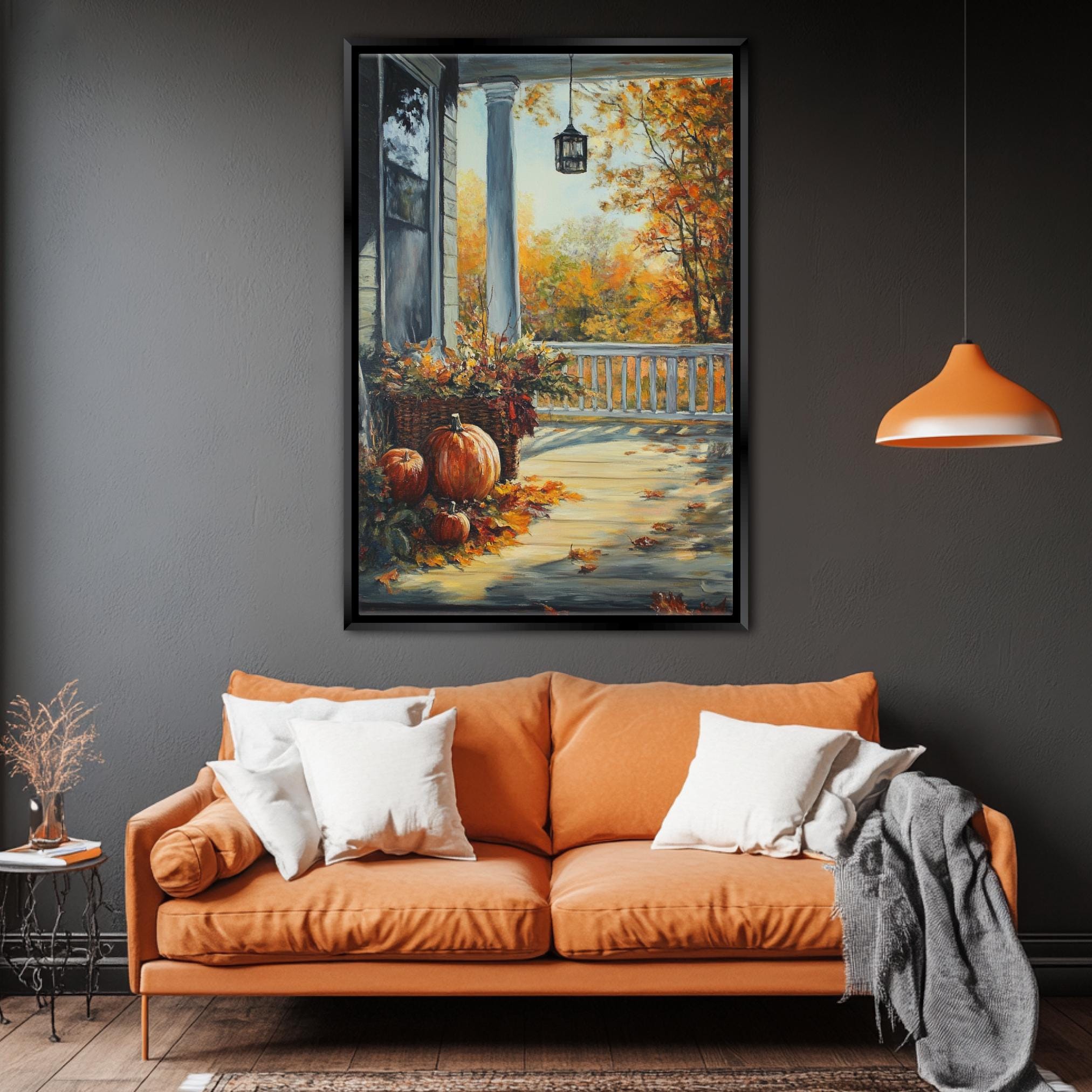 a cozy living room with a large orange sofa adorned with white pillows, a framed painting of a porch with pumpkins and fall foliage hanging on the wall, and a hanging lamp providing soft lighting.