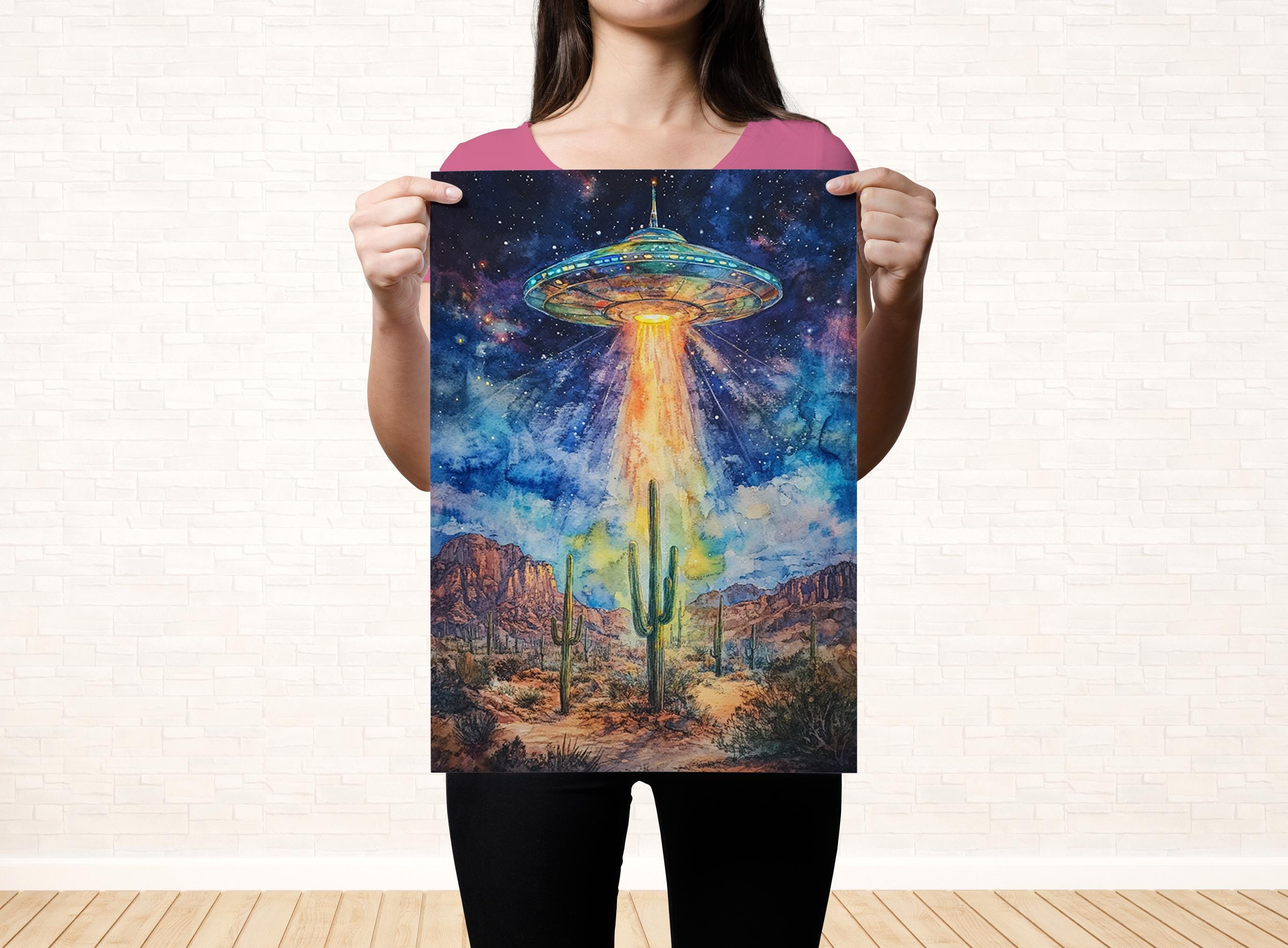 A woman holds up a poster featuring a colorful, surreal scene of an alien spacecraft hovering over a desert landscape with cacti and mountains in the background.