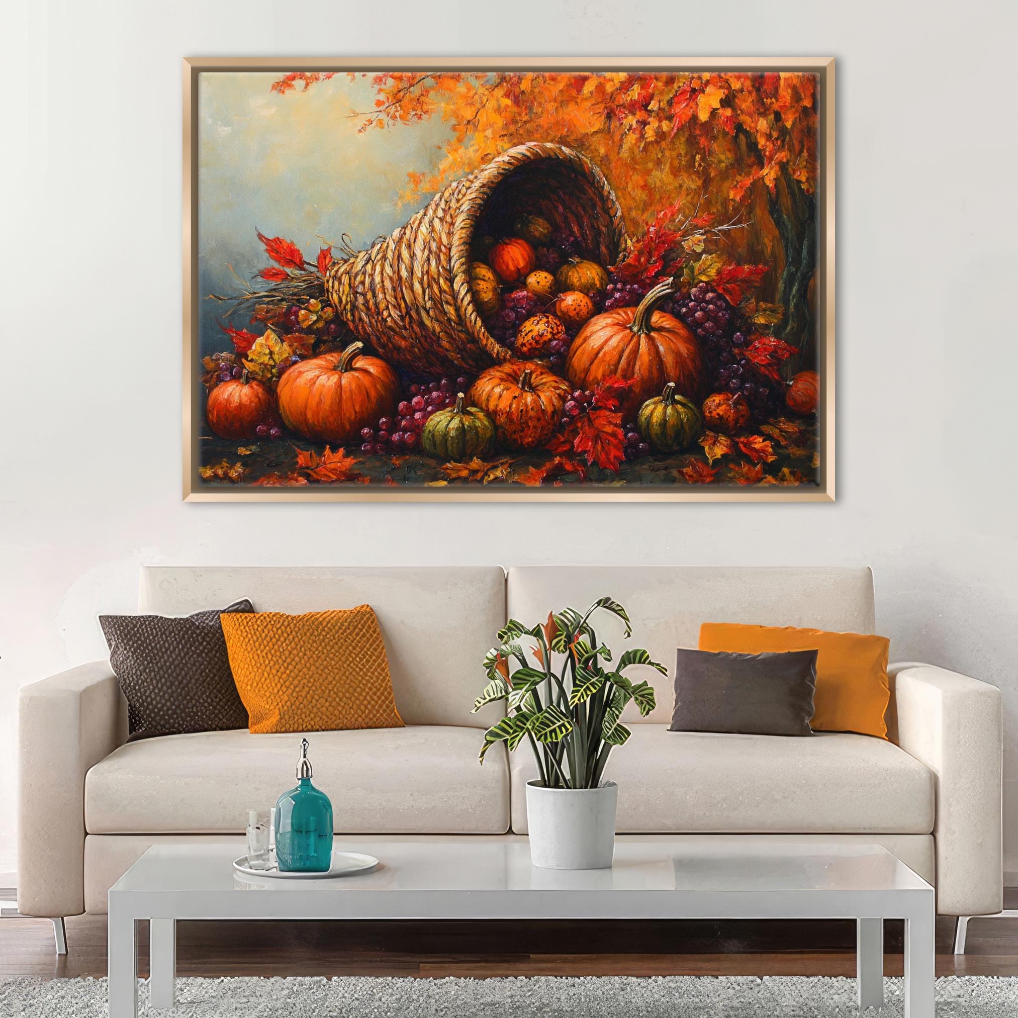 a cozy living room with a white sofa adorned with orange and brown throw pillows. Above the sofa, a large painting of a cornucopia filled with autumn fruits and vegetables, including pumpkins, grapes, and apples, hangs on the wall. The painting is framed in gold, adding a touch of elegance to the room. In front of the sofa, there is a coffee table with a blue vase and a plant, contributing to the warm and inviting atmosphere of the space.