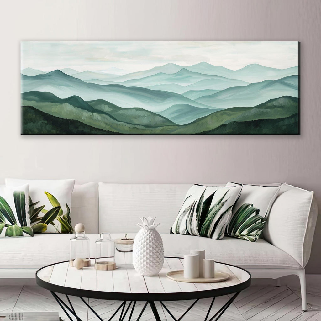 a large landscape painting hanging on a wall above a white sofa with green and white throw pillows. In front of the sofa, there is a coffee table with a pineapple vase, candles, and other decorative items.