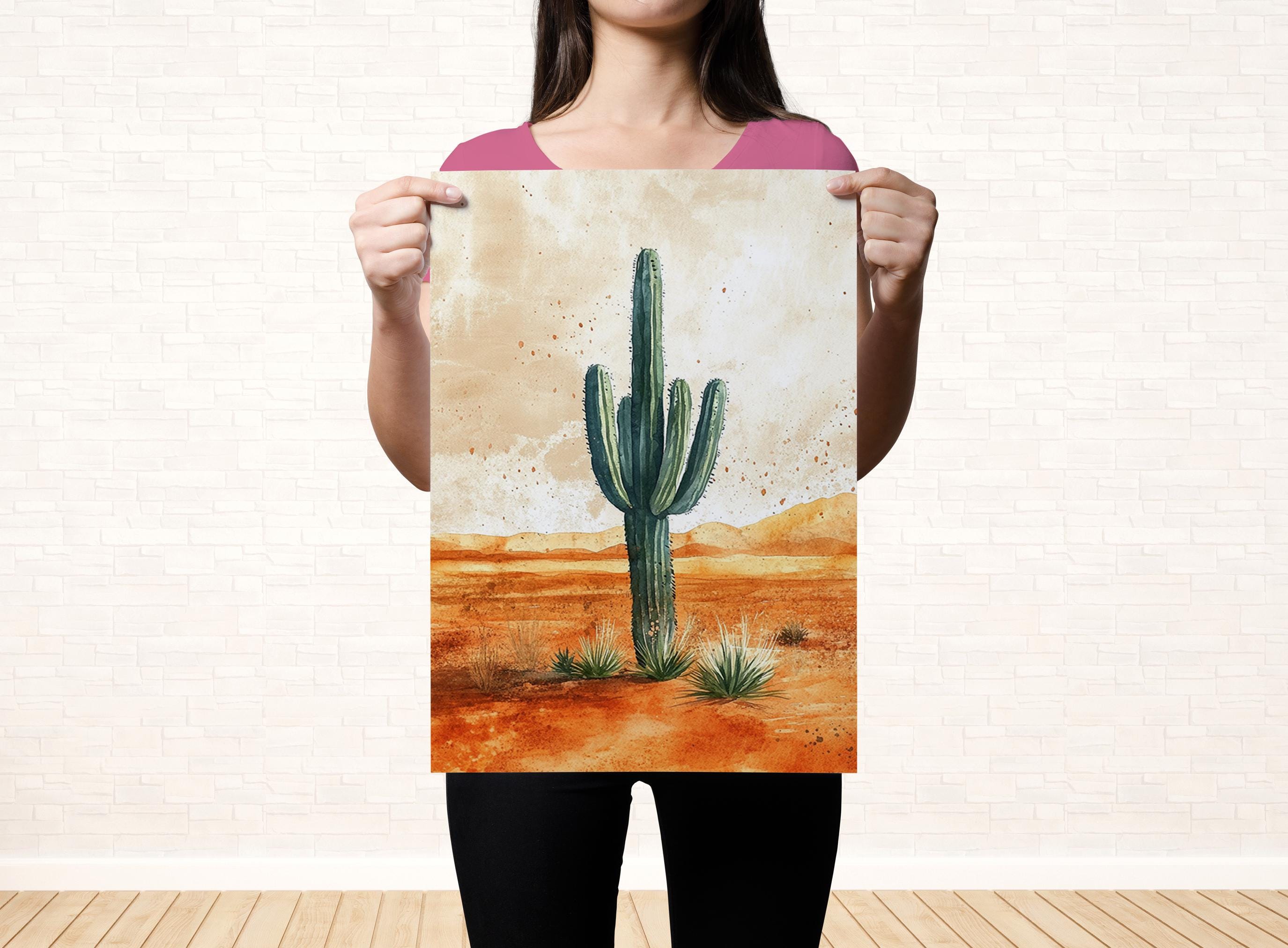 A woman holds up a framed print of a desert scene with a cactus in the foreground.