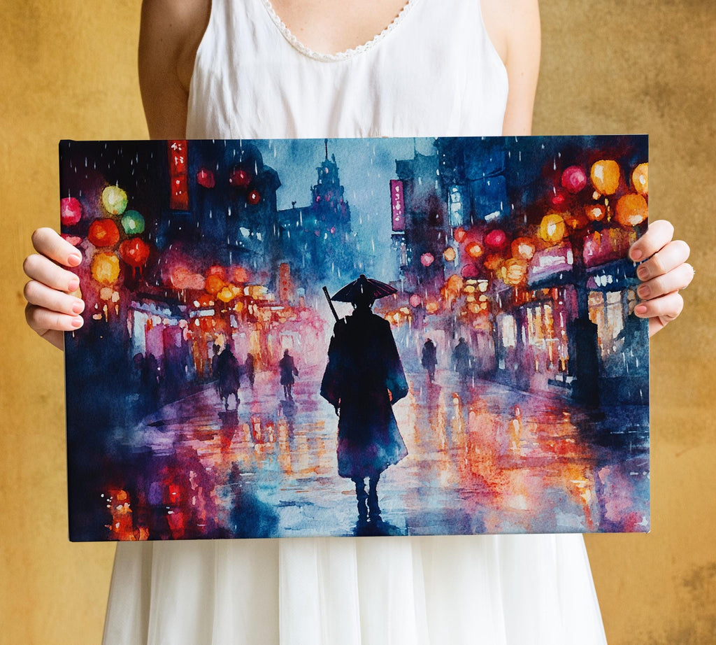 A person is holding a framed painting depicting a city street scene at night, with colorful lights and a lone figure walking down the wet street.
