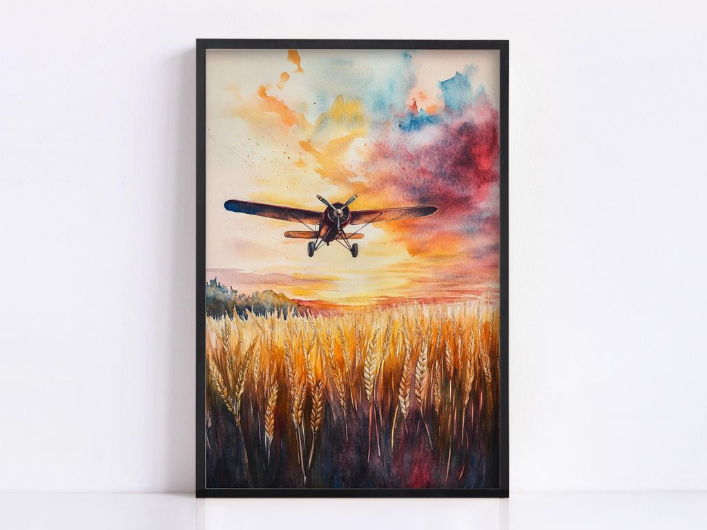 A framed watercolor painting depicting a small airplane flying over a field of golden wheat against a vibrant sunset sky.