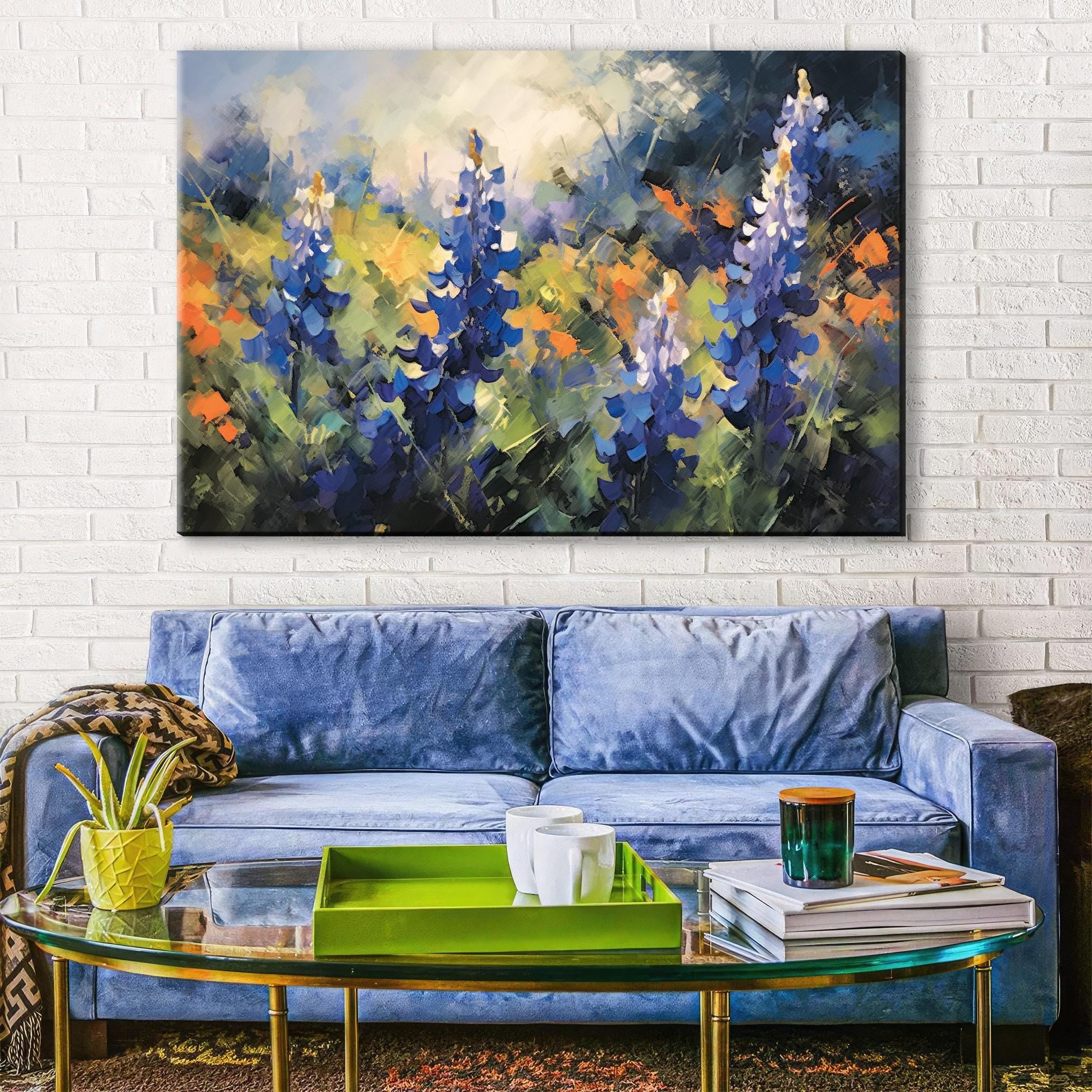 a large painting of blue flowers hanging on a white brick wall above a blue velvet sofa in a living room setting.