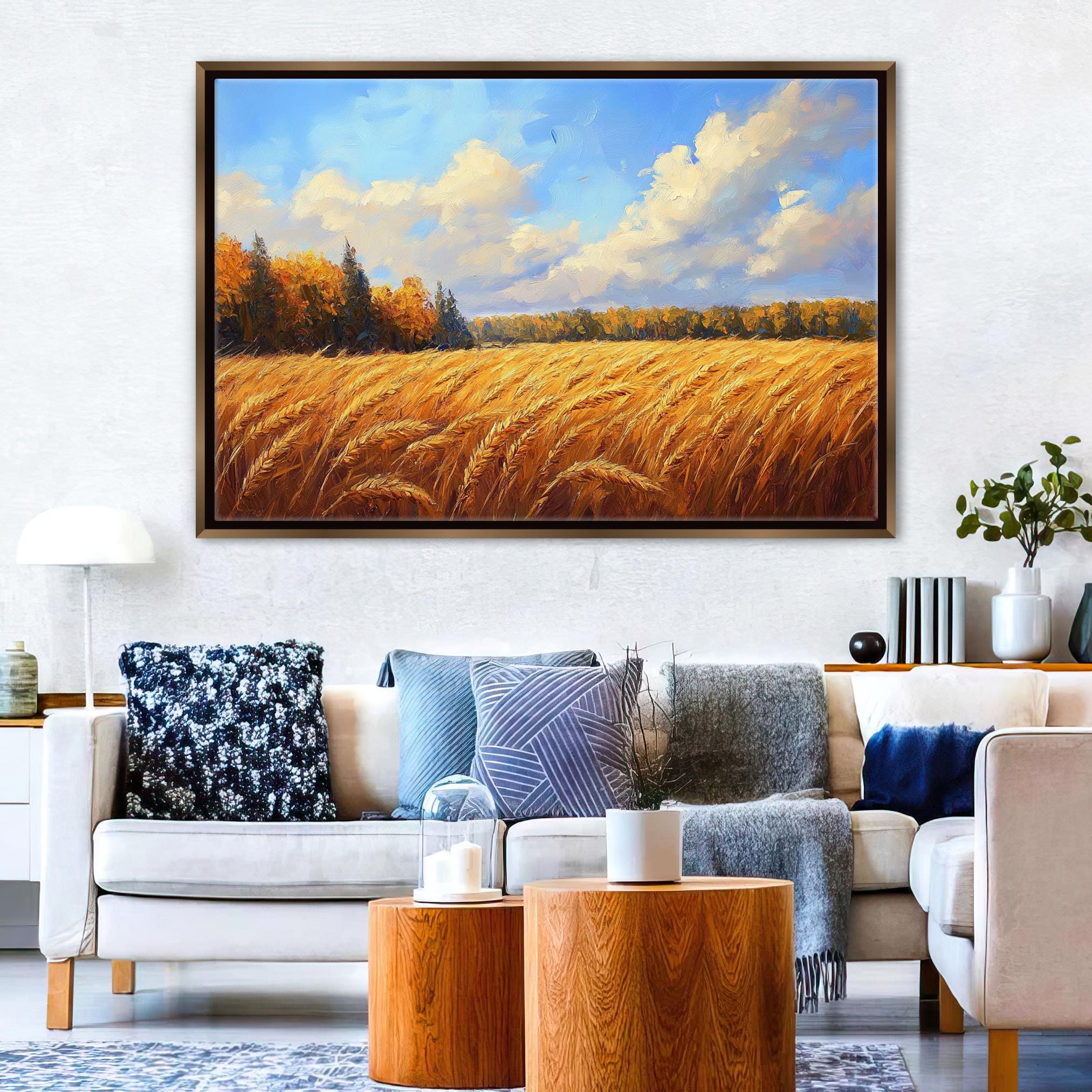 a large painting of a field of golden wheat against a blue sky with clouds, hanging on a wall above a white sofa with various throw pillows.