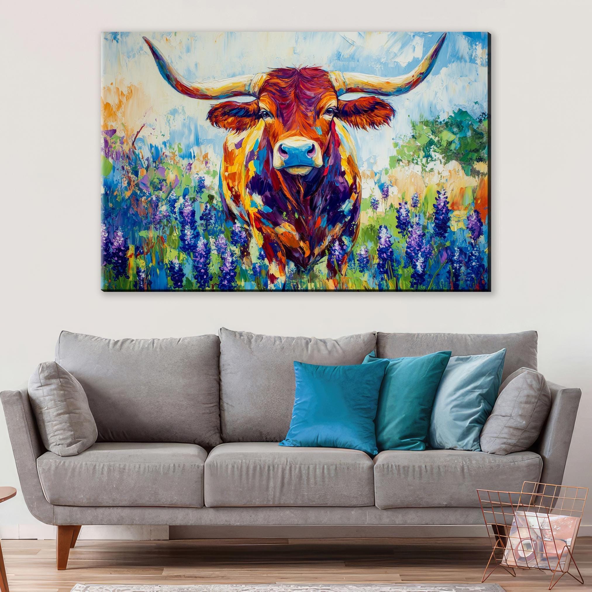 a large, colorful painting of a bull with horns hanging on a wall above a gray couch with blue pillows.
