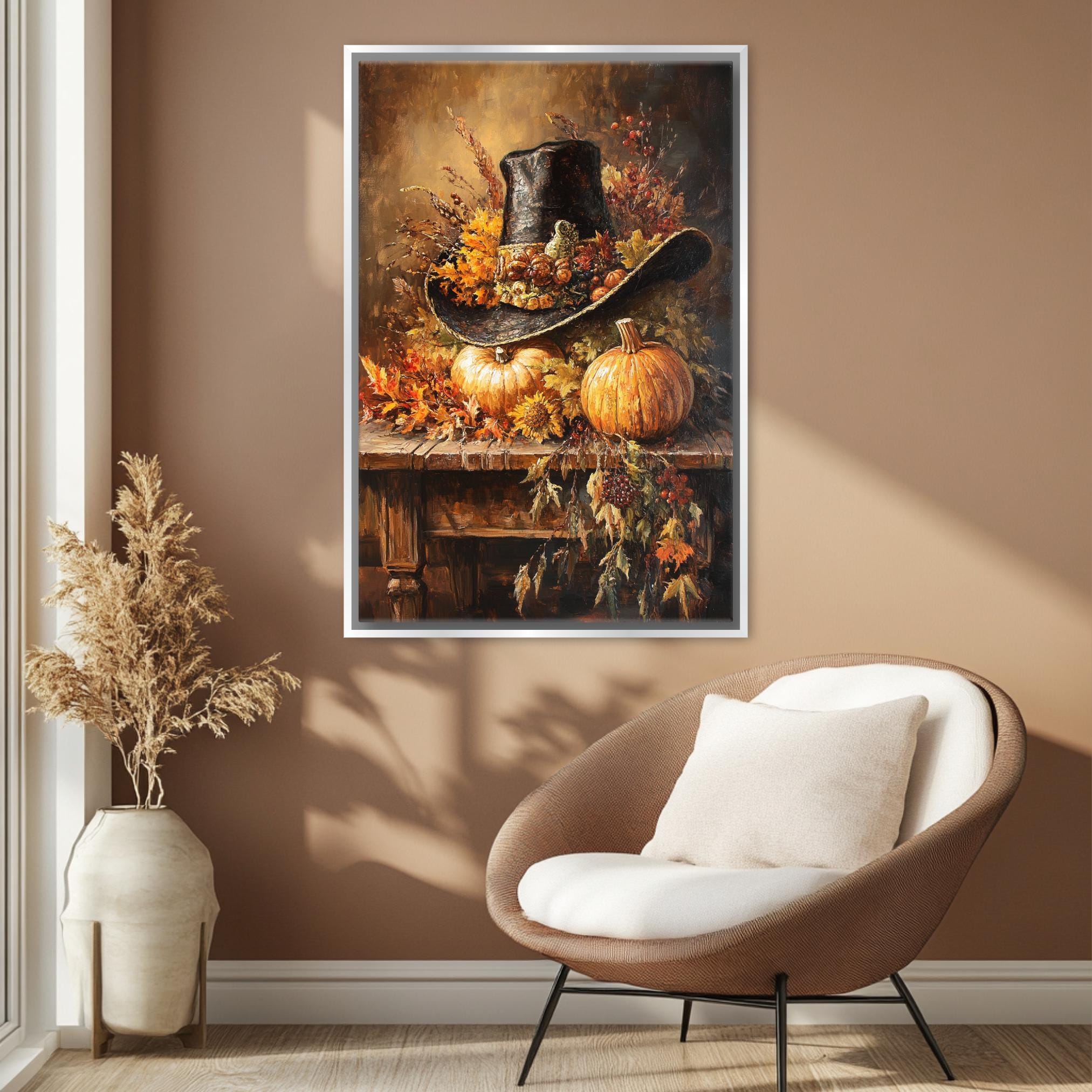 a framed painting of a cowboy hat, pumpkins, and autumn foliage hanging on a wall in a room with a brown chair and a potted plant.