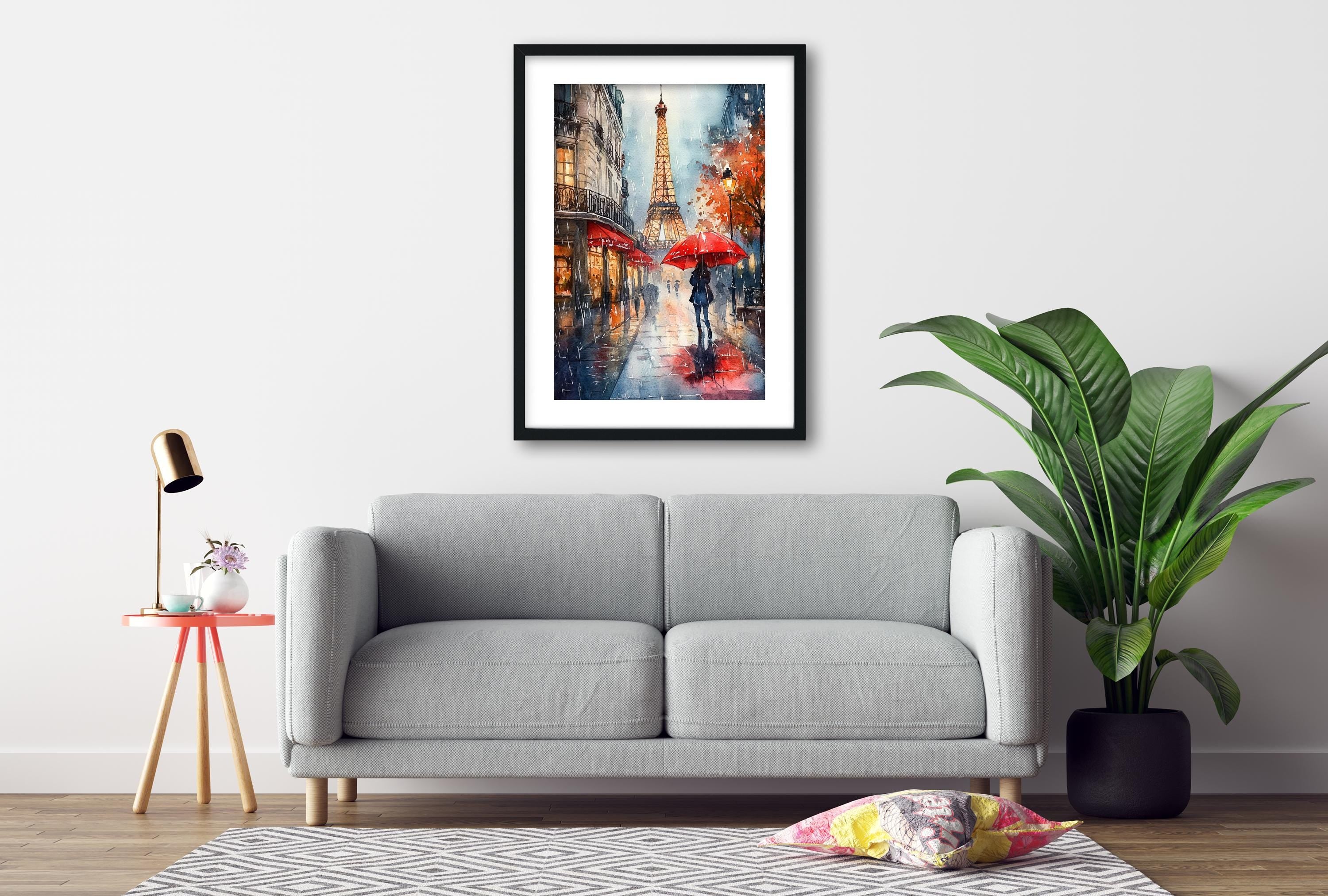 a gray sofa, a framed painting of a rainy city street with a tall tower, a red umbrella, and a potted plant, all set against a white wall.