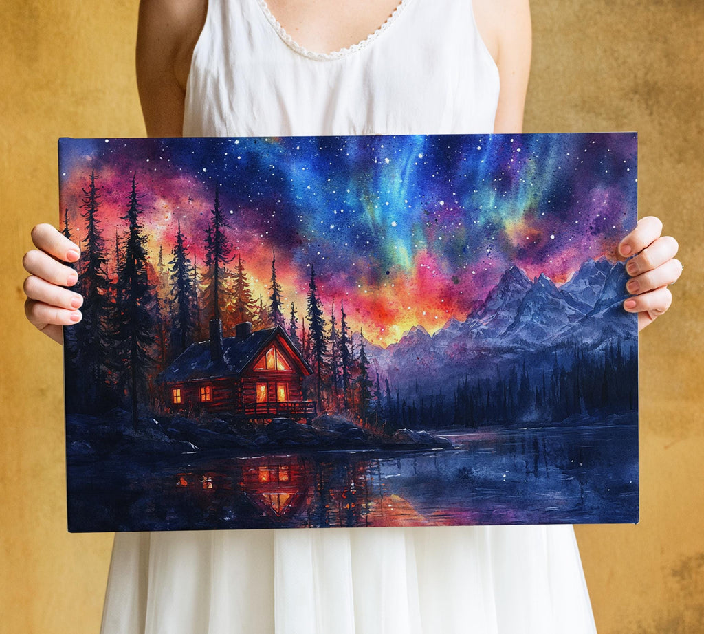 A person is holding up a framed painting depicting a serene landscape with a cabin nestled among pine trees, a lake reflecting the vibrant colors of the night sky, and mountains in the background.