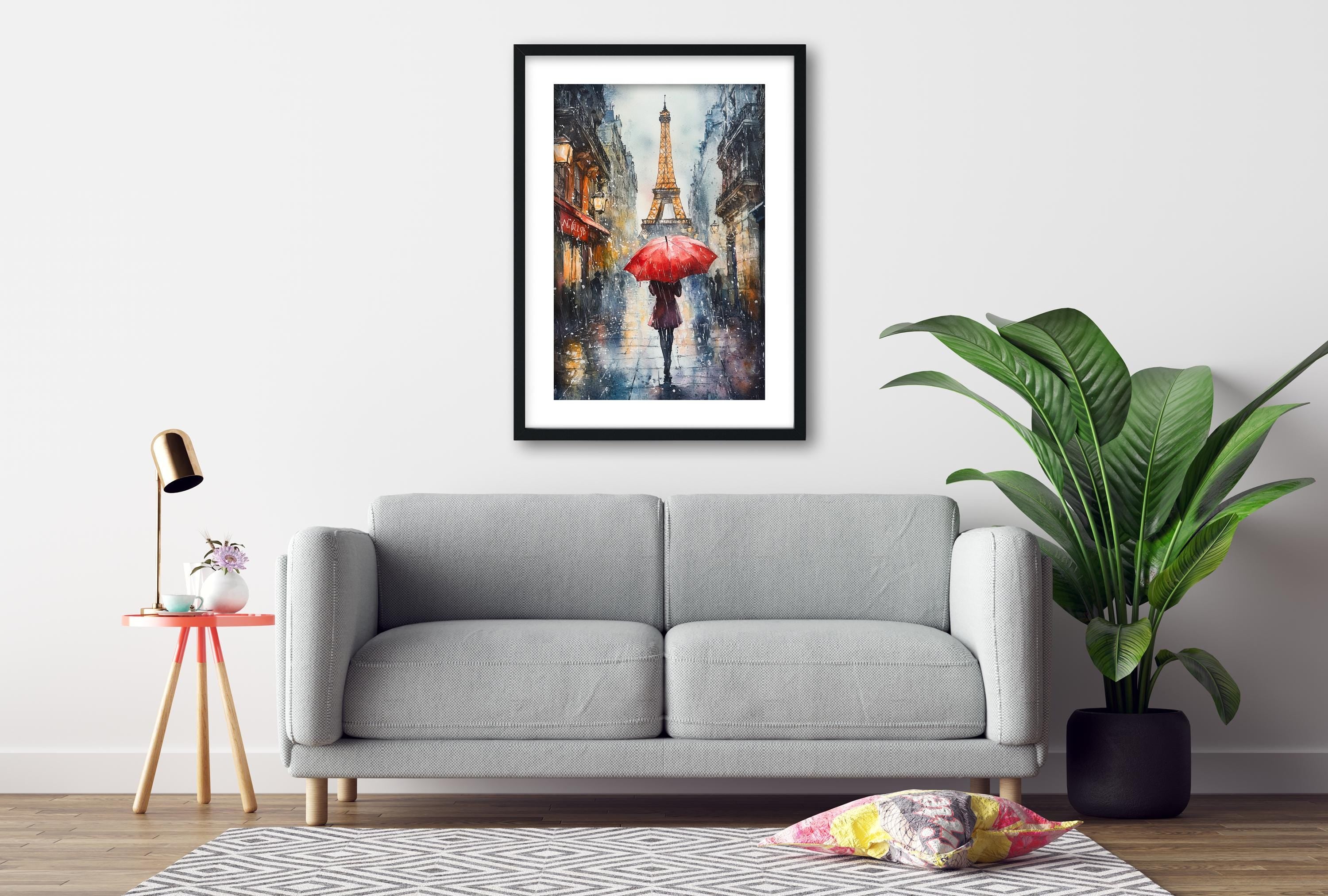 a gray sofa, a framed painting of a rainy street scene with a red umbrella, a small table with a lamp, and a potted plant.