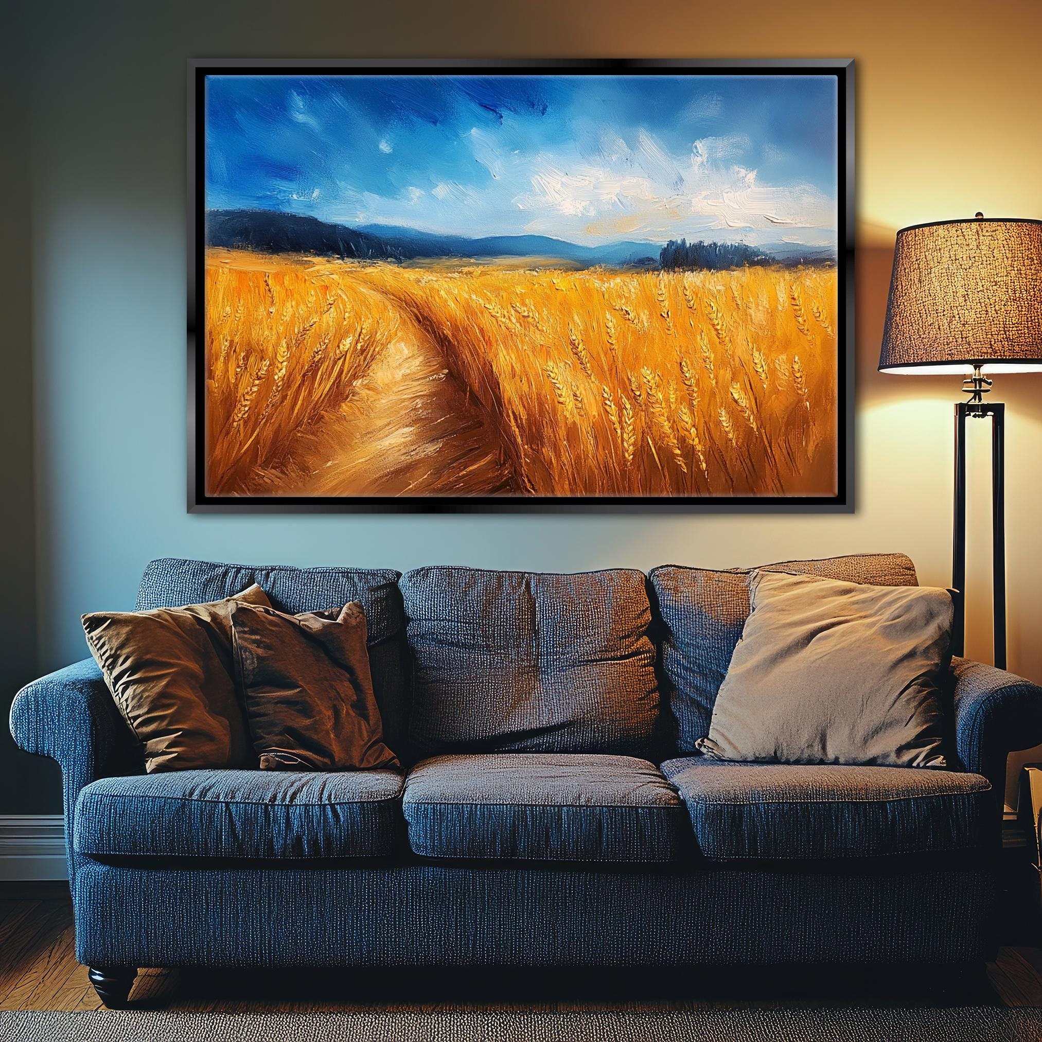 a large painting of a field of golden wheat hanging on a wall above a blue couch with pillows.
