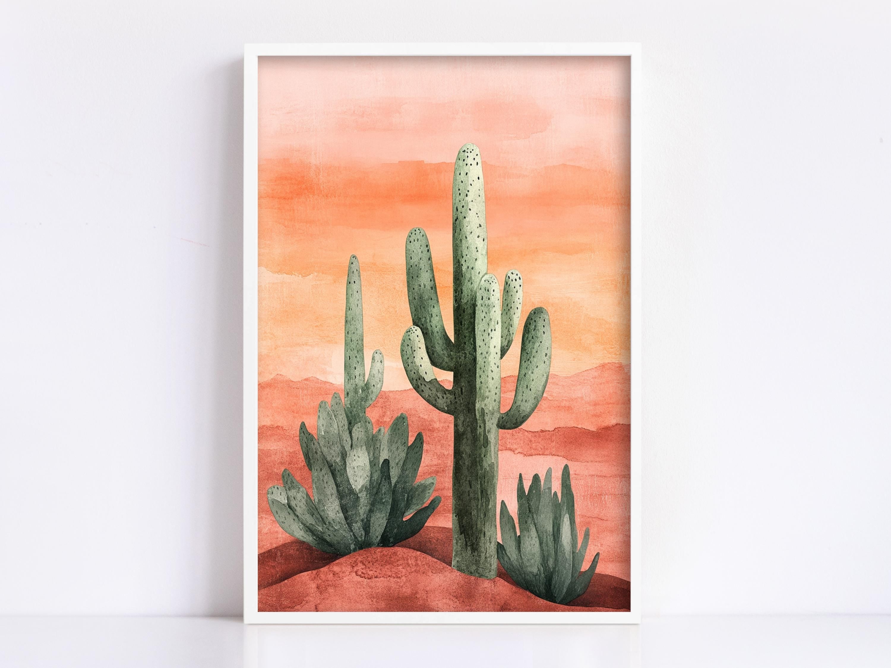 A framed watercolor painting depicting a desert landscape with three cacti against a warm orange and red background.