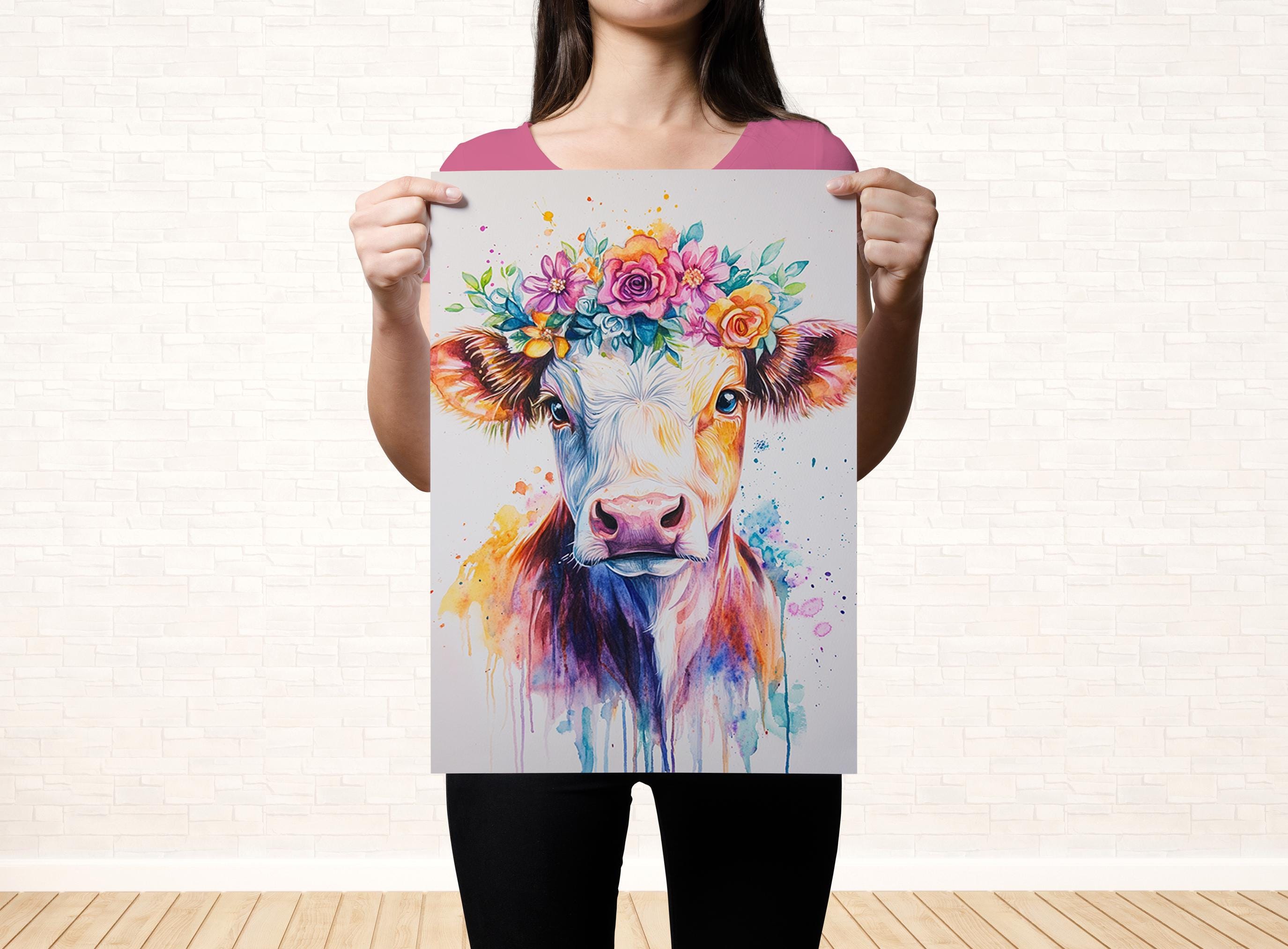 A woman is holding up a colorful painting of a cow with a flower crown on its head.
