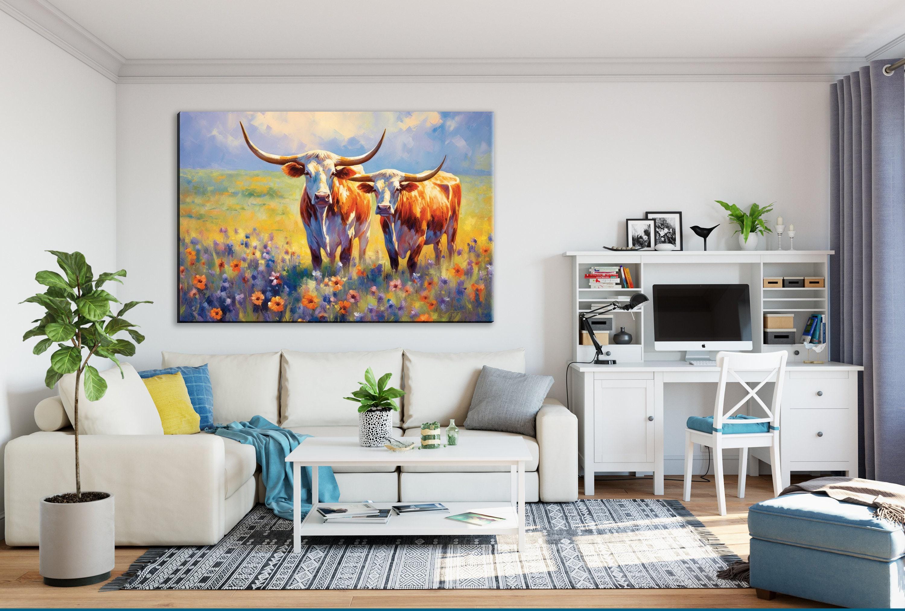 a cozy living room with a large painting of two cows in a field hanging on the wall. The room is furnished with a white sofa, a coffee table, and a desk with a computer setup. The room also features a potted plant, a vase, and a bookshelf, creating a warm and inviting atmosphere.