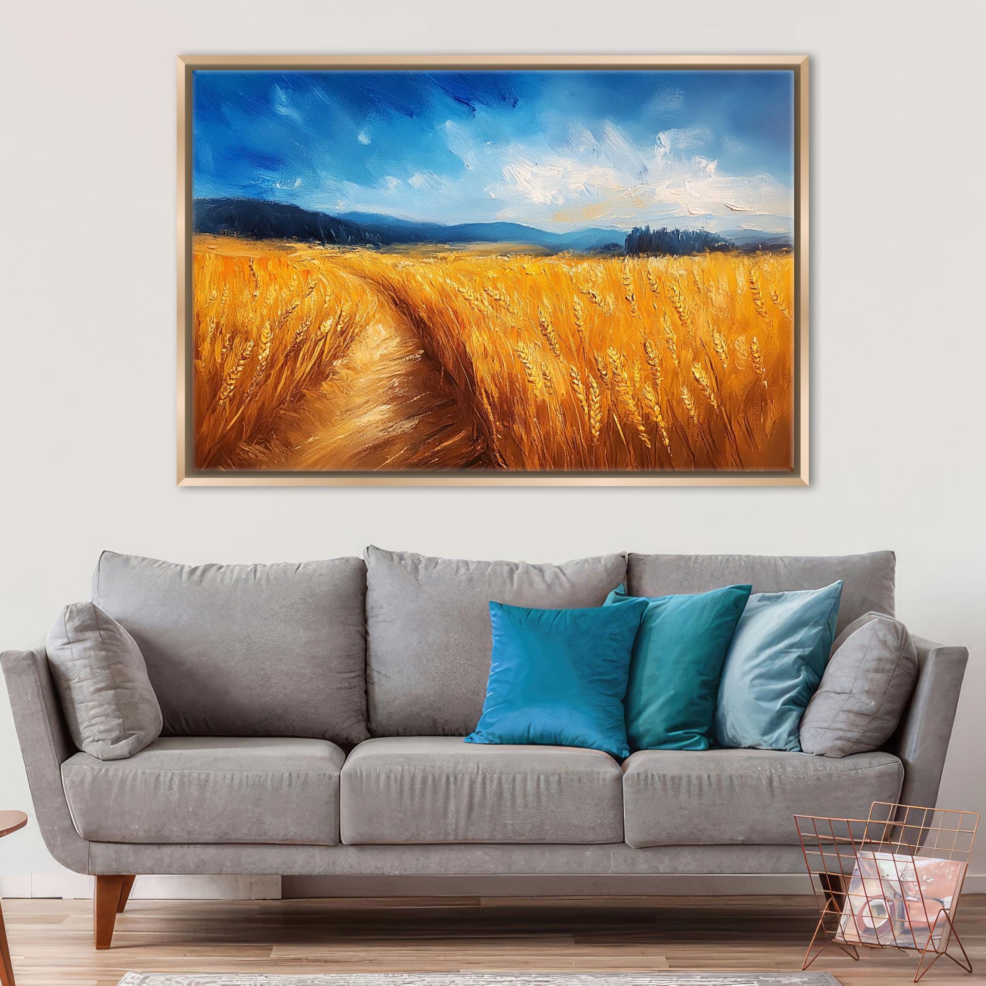 a large painting of a field of golden wheat hanging on a wall above a gray sofa with blue and teal throw pillows.