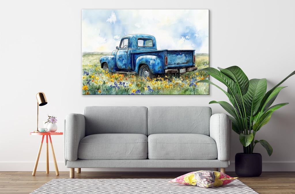 a cozy living room with a gray sofa, a small table with a lamp, and a large painting of an old blue pickup truck in a field of flowers hanging on the wall above the sofa.
