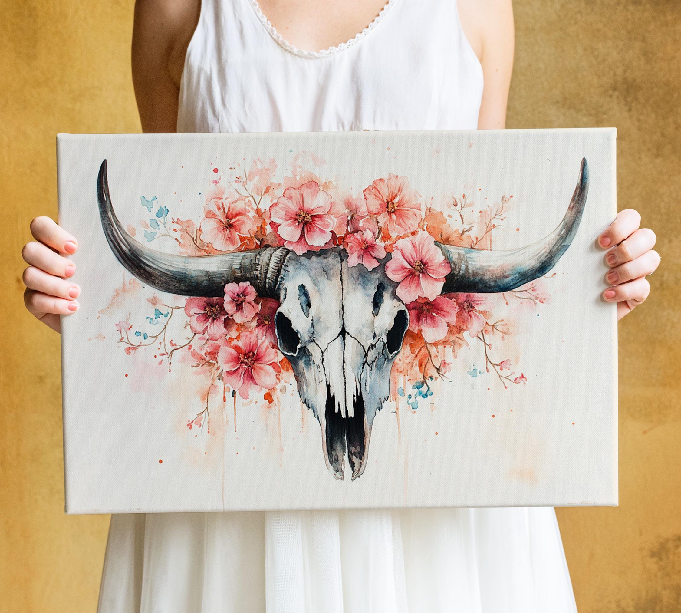 A woman holds a canvas featuring a detailed illustration of a skull with large horns and a floral design.