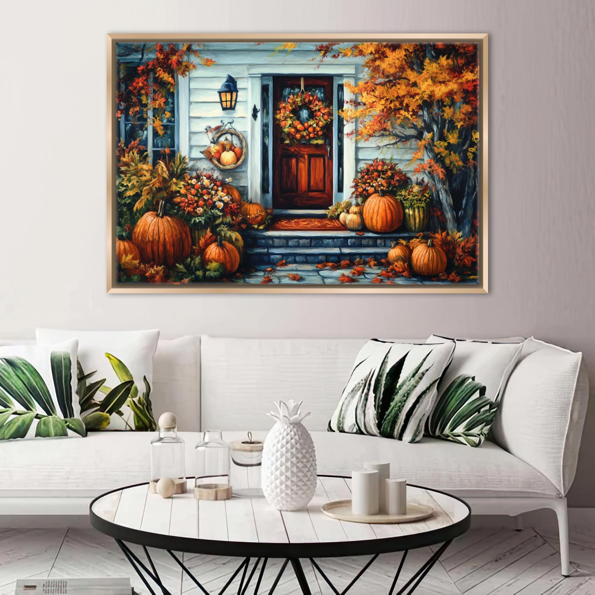 a cozy living room with a large painting of a house and porch adorned with pumpkins and fall foliage hanging on the wall above a white sofa with throw pillows.
