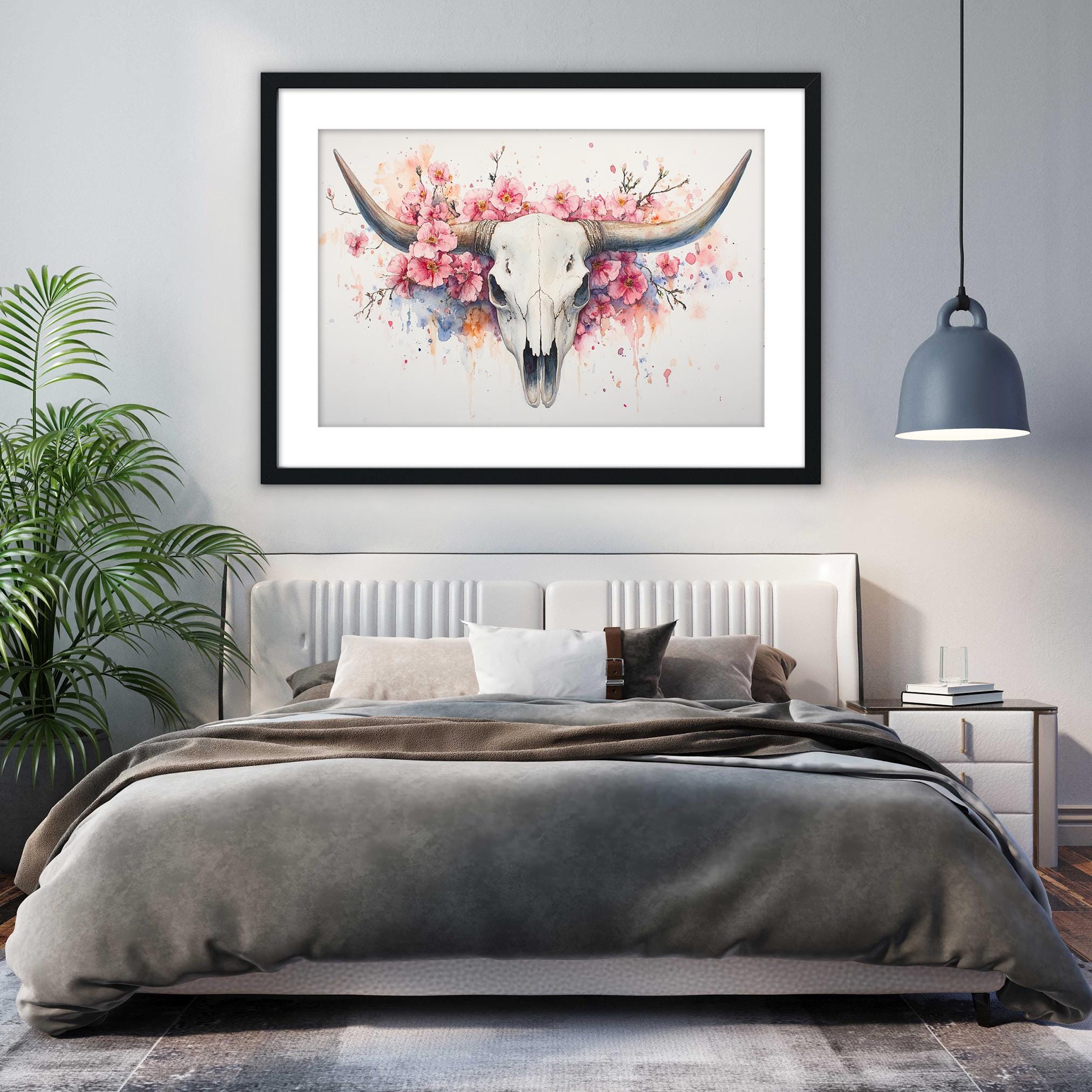 a bedroom with a large bed, a framed artwork of a bull's skull with flowers hanging above it, and a potted plant to the left.