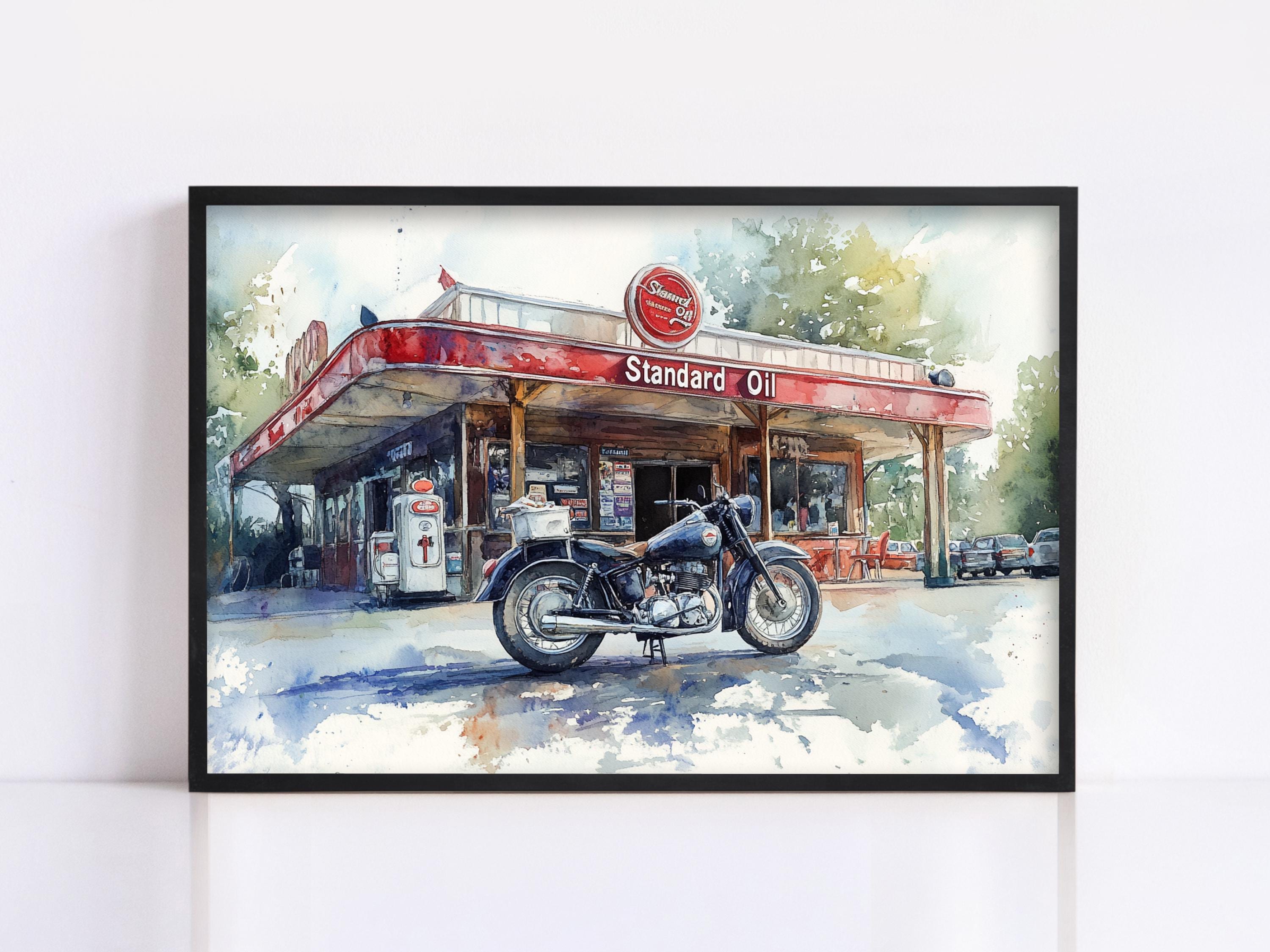A framed painting depicting a classic motorcycle parked in front of a Standard Oil gas station.