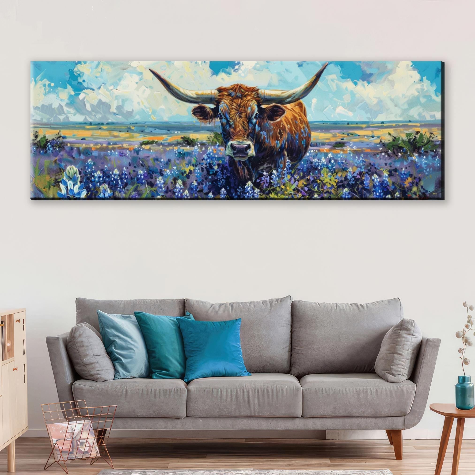 a large painting of a bull with long horns, set against a backdrop of a field with purple flowers. The painting is hanging on a wall above a gray couch with blue pillows.