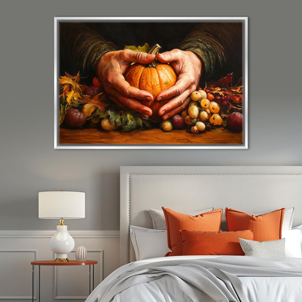 A framed painting of a pair of hands holding a pumpkin is displayed above a bed with orange pillows and a white headboard.