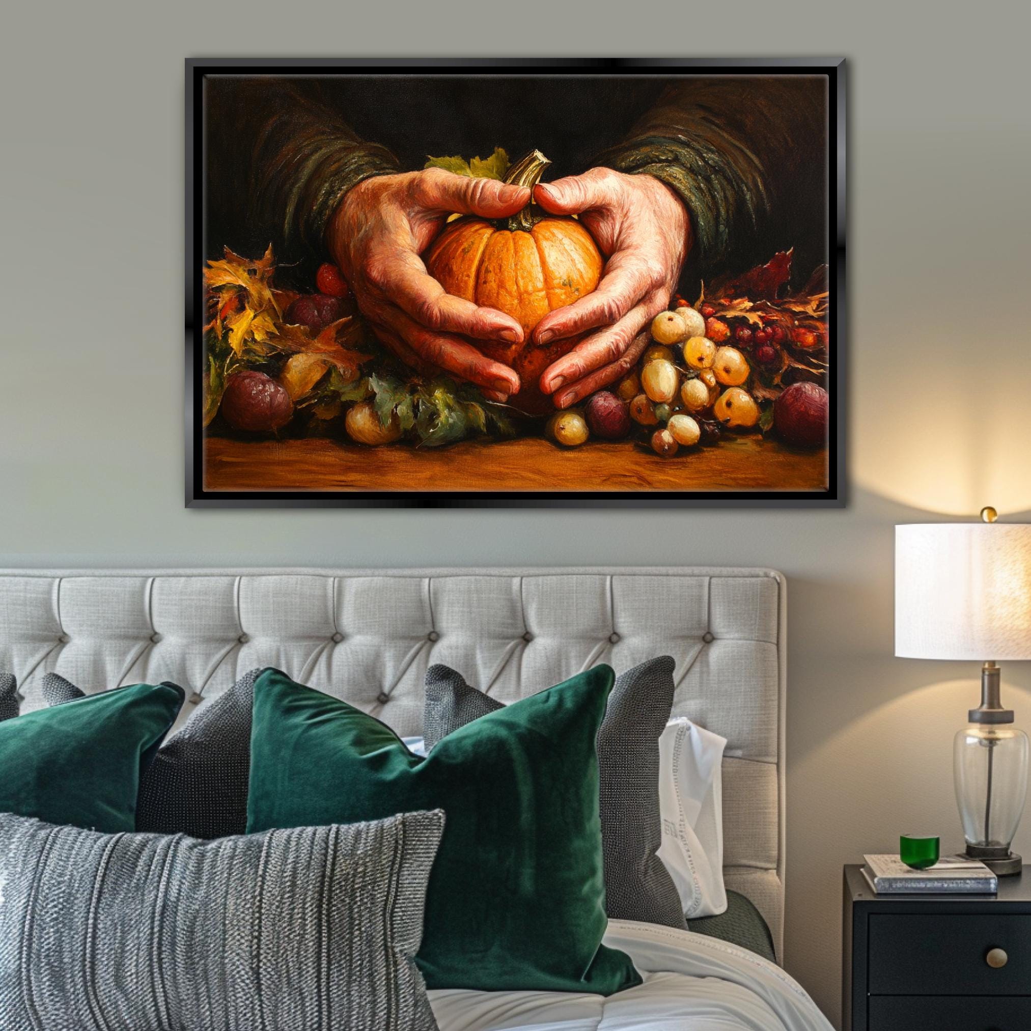 A framed painting of a pair of hands holding a pumpkin is displayed on a wall above a bed with green pillows.