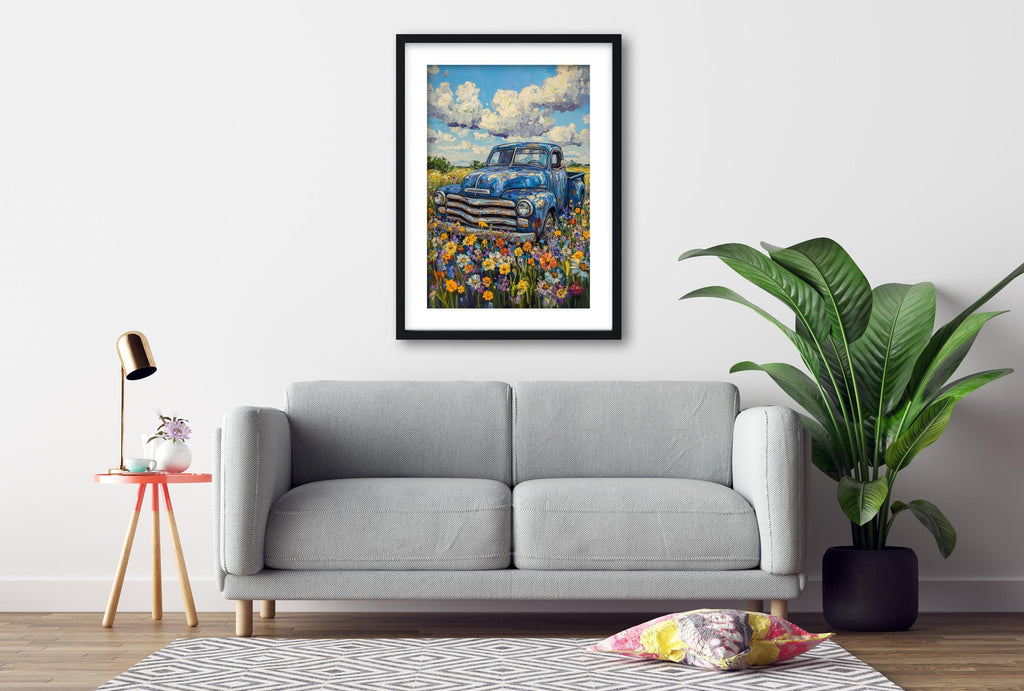 a gray sofa, a framed painting of a blue truck in a field, a small table with a lamp, and a potted plant, all arranged in a living room setting.