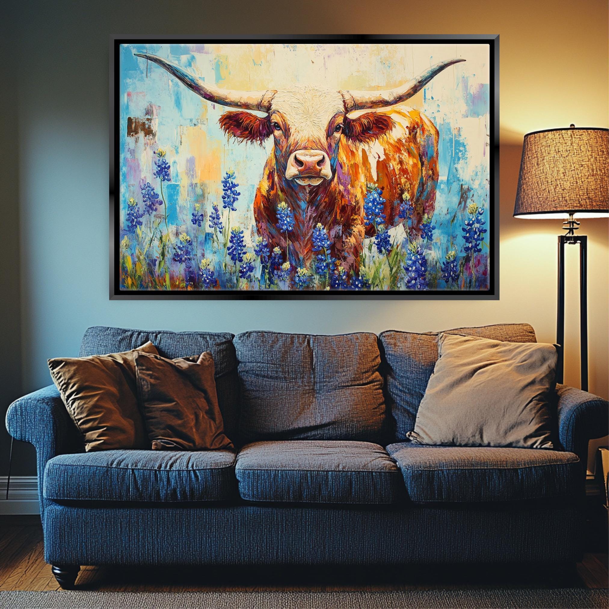 a large painting of a bull with horns, surrounded by blue flowers, hanging on a wall above a blue couch with pillows.