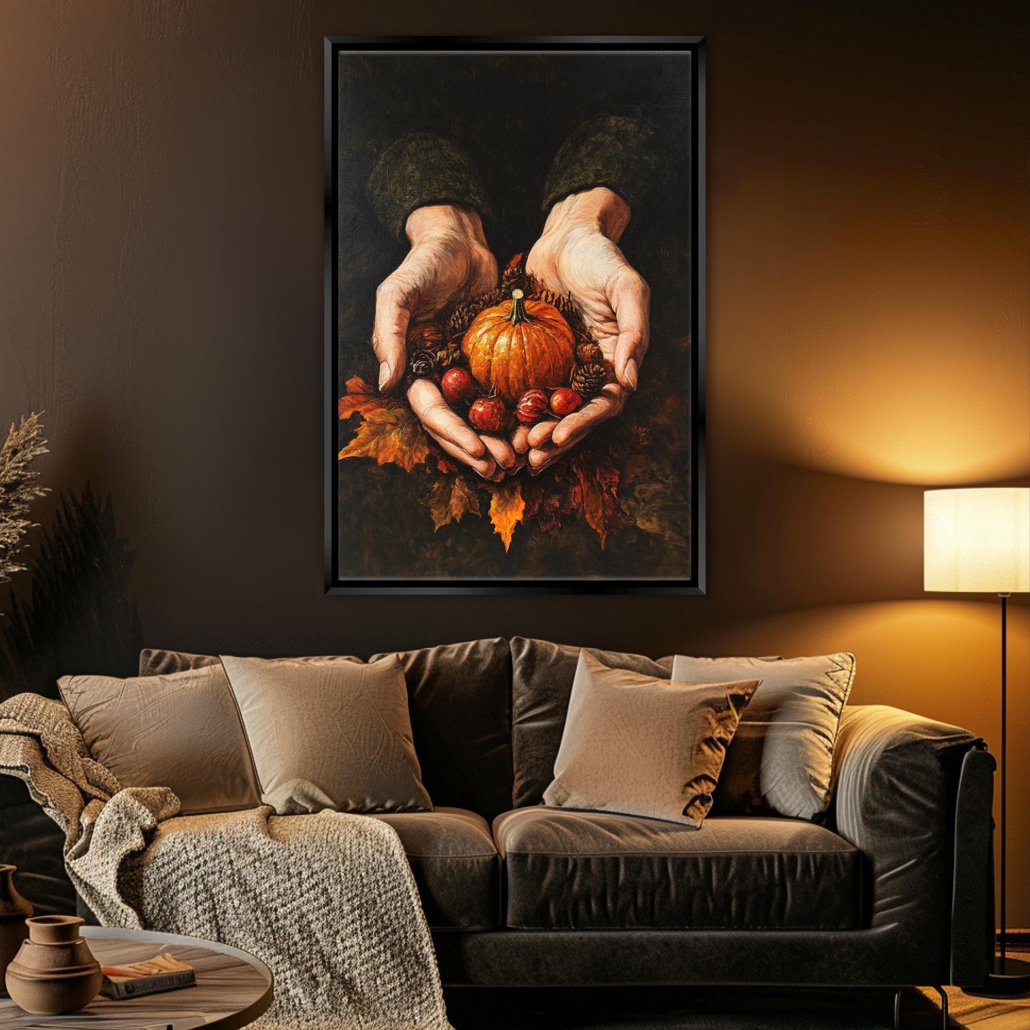 A cozy living room with a brown leather couch, a lamp, and a framed painting of a pair of hands holding a pumpkin and autumn leaves.