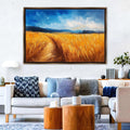 a large painting of a golden wheat field hanging on a wall above a white sofa with various throw pillows.