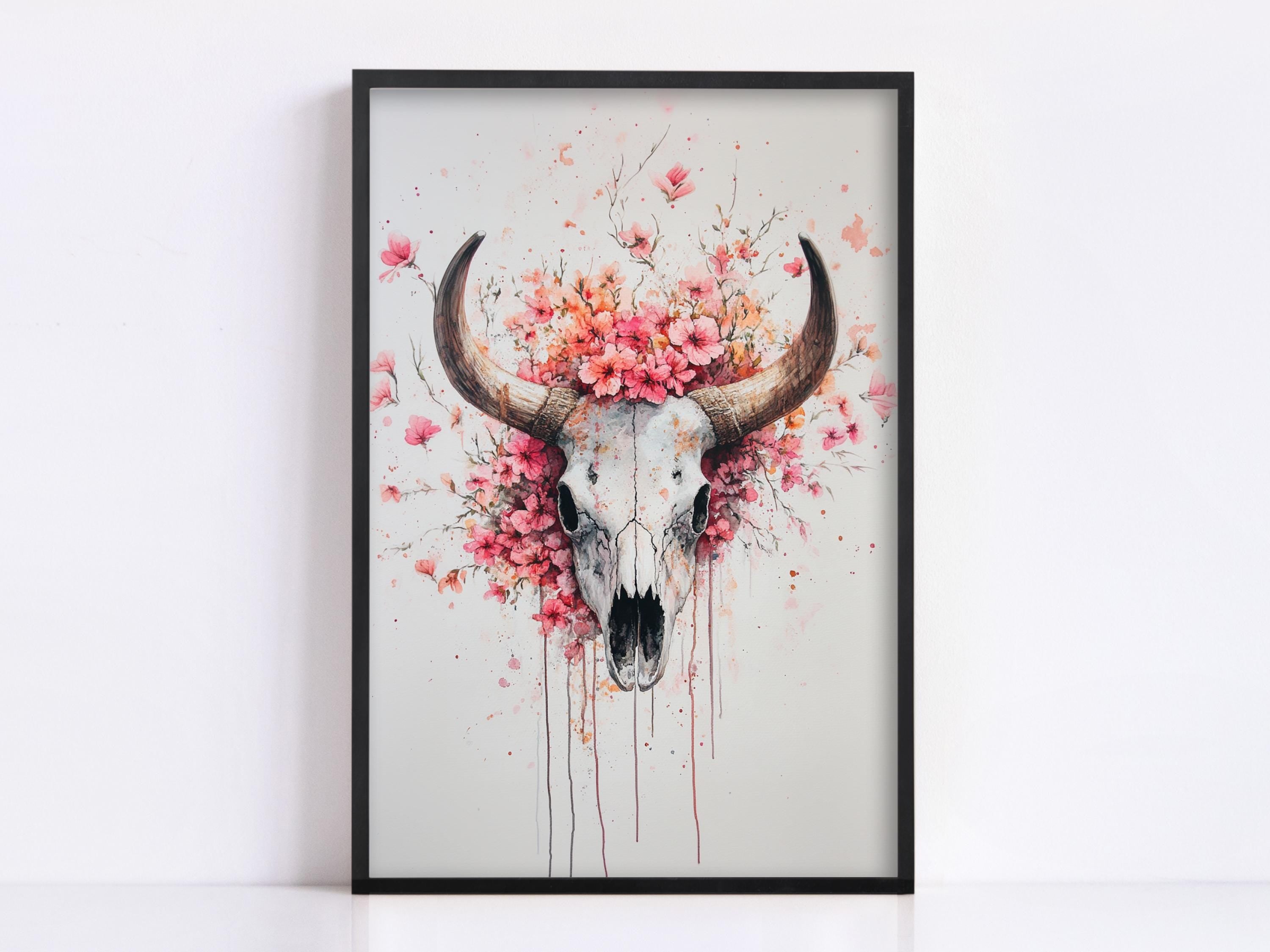 a framed artwork depicting a skull with large horns, surrounded by a floral arrangement of pink flowers.