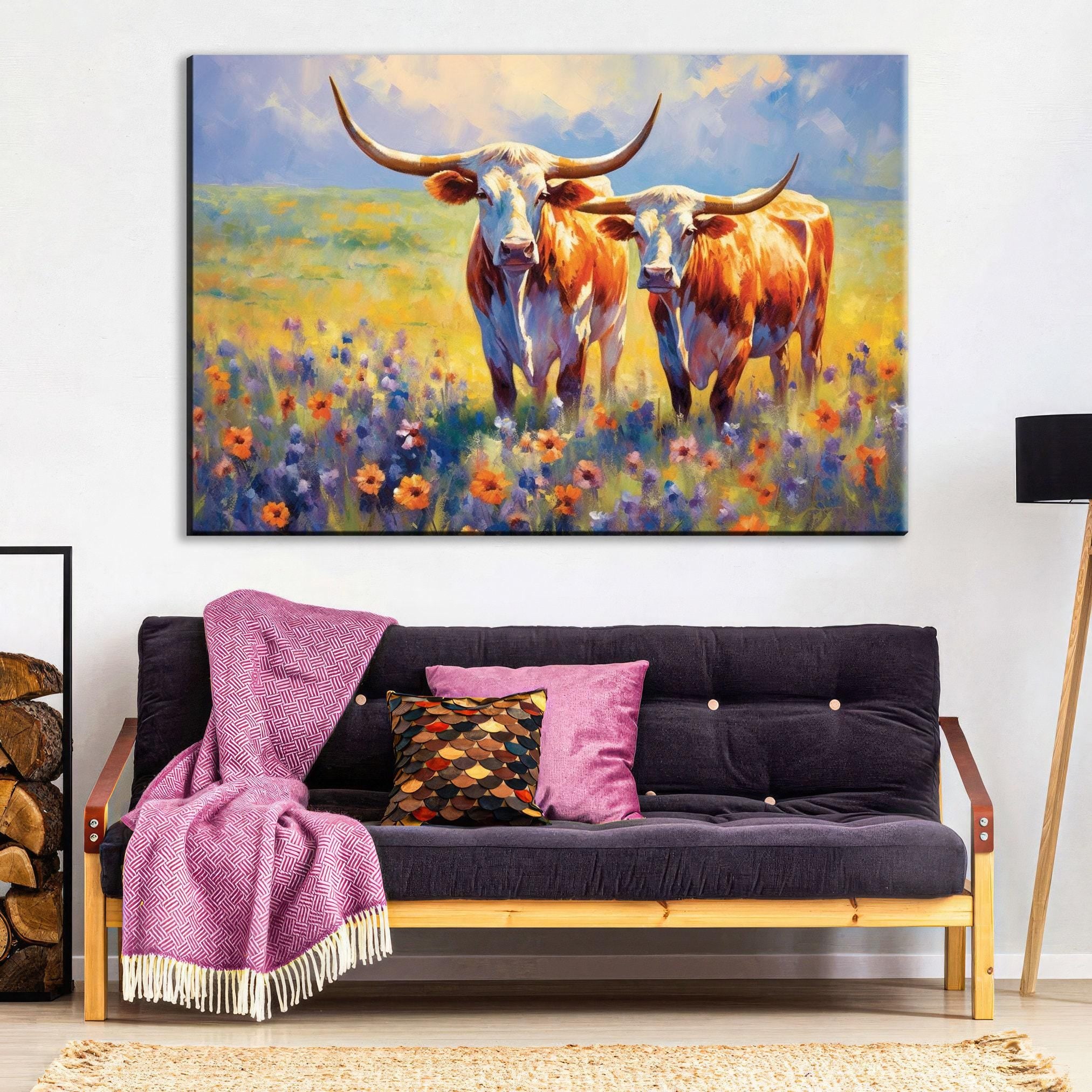 a large painting of two longhorn cattle standing in a field of flowers, with a purple blanket and throw pillow on a couch in the foreground.
