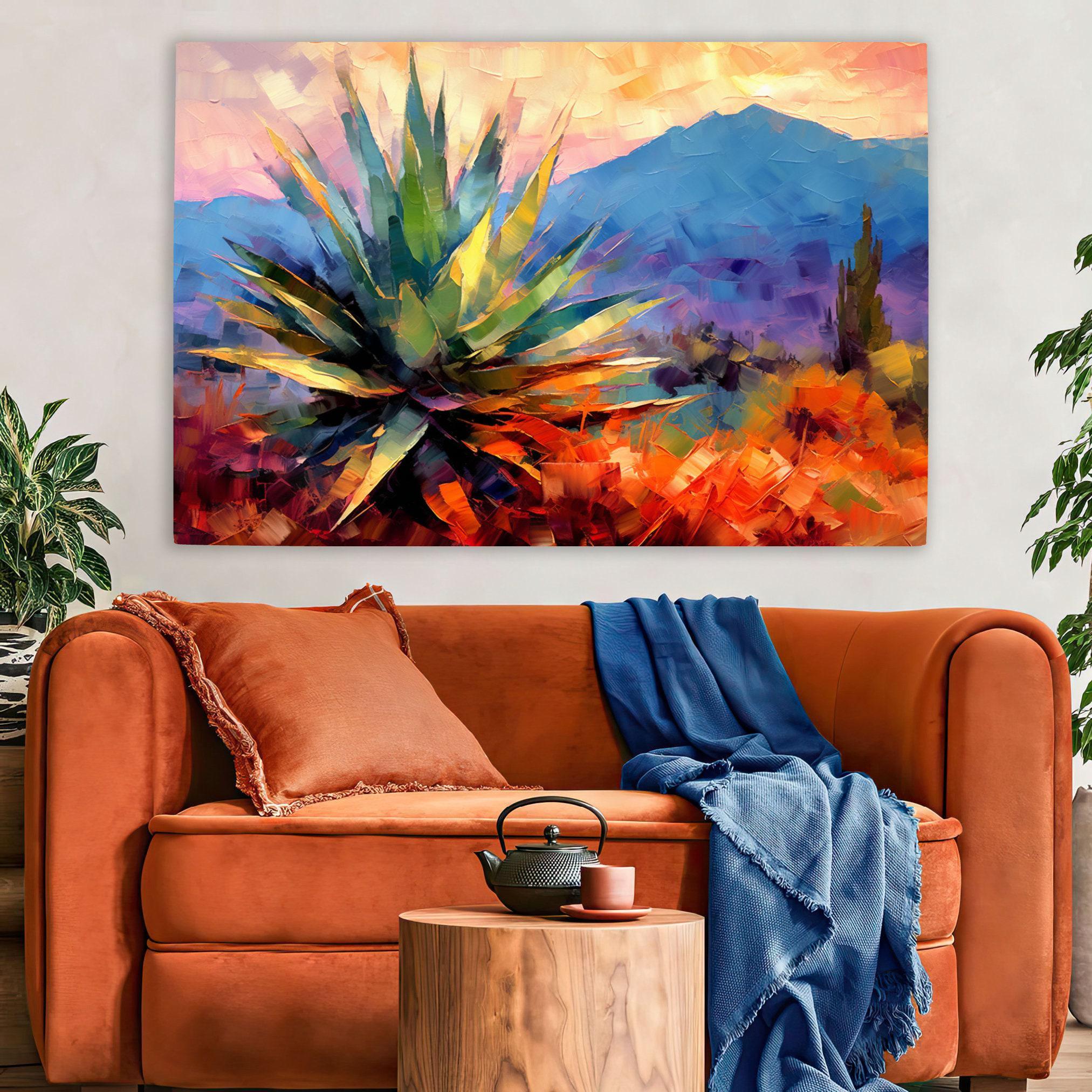 a large, colorful painting of a desert landscape with a prominent cactus in the foreground. The painting is displayed on a wall above a cozy living room setting with a brown sofa, a wooden side table, and a potted plant.